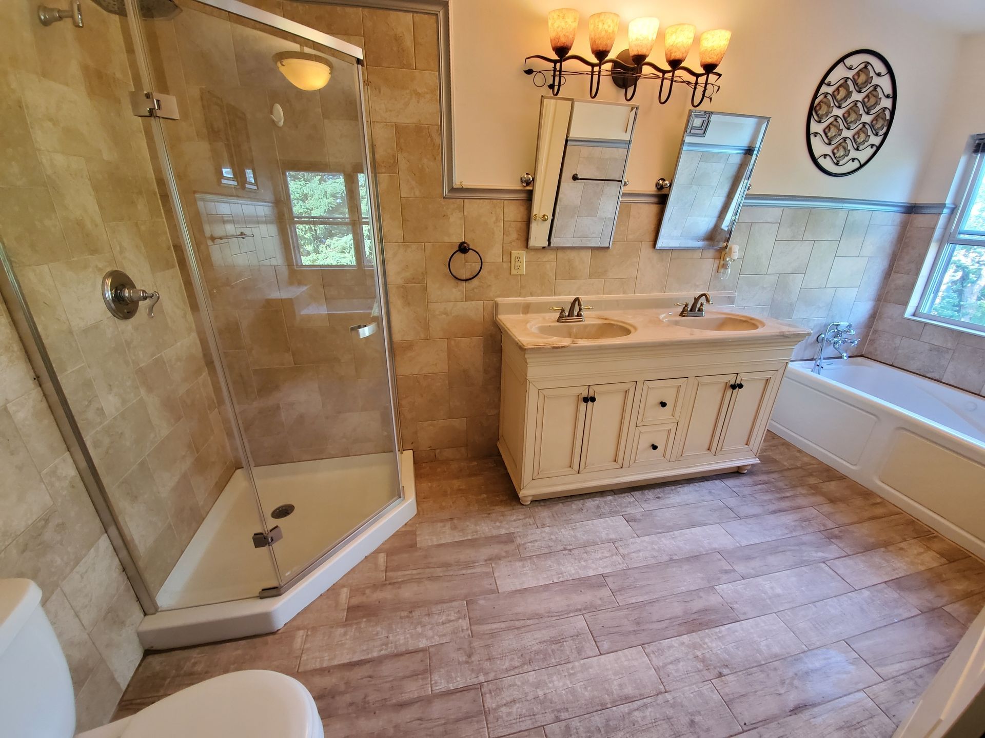 Bathroom with beige tile, glass shower, double vanity, and a toilet.