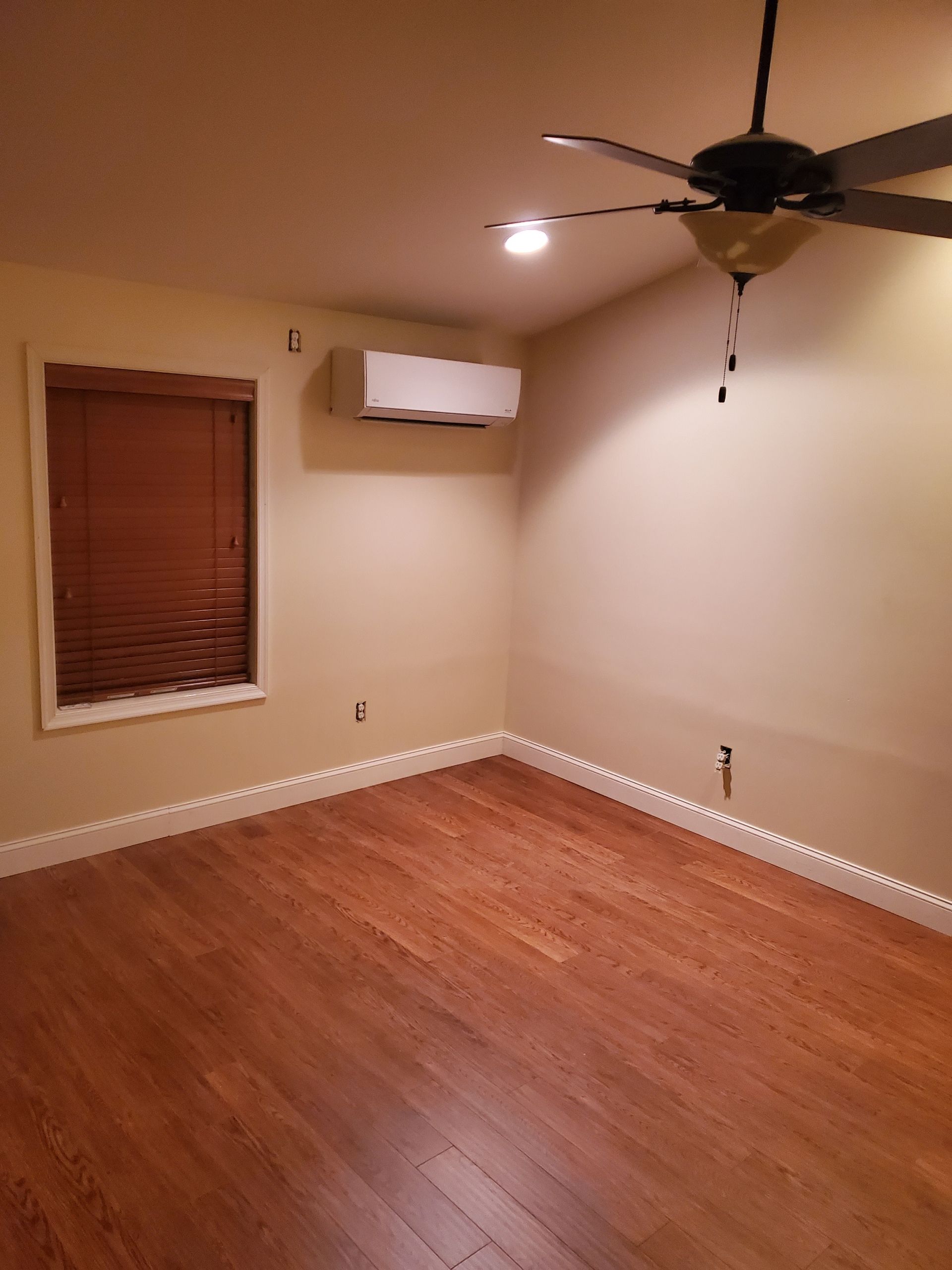 Empty room with hardwood floors, a window with blinds, and a mounted air conditioner.