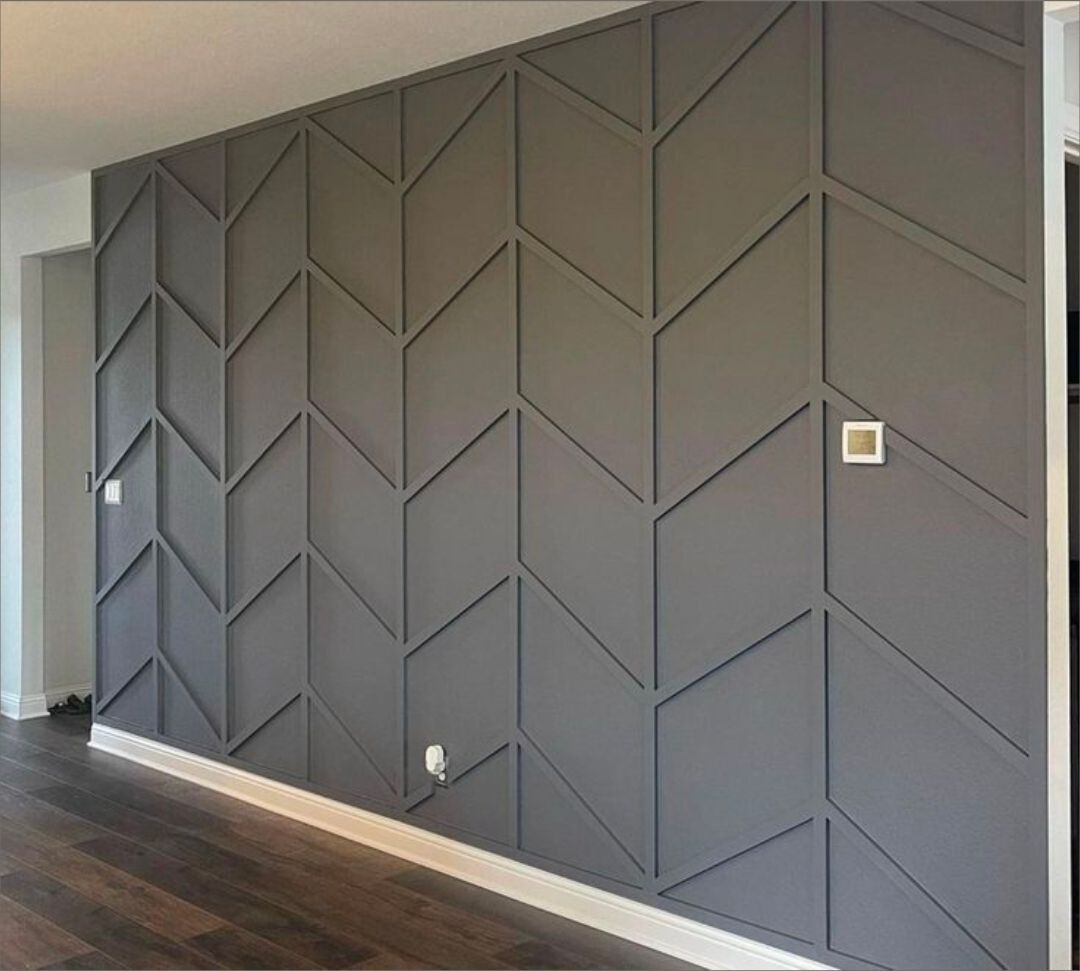 Dark gray geometric accent wall with angled panels in a modern room and dark wood floor