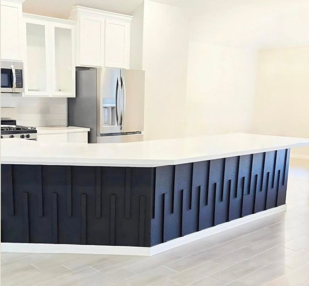 Modern kitchen with white cabinets, stainless steel fridge, and a dark blue island with vertical slats