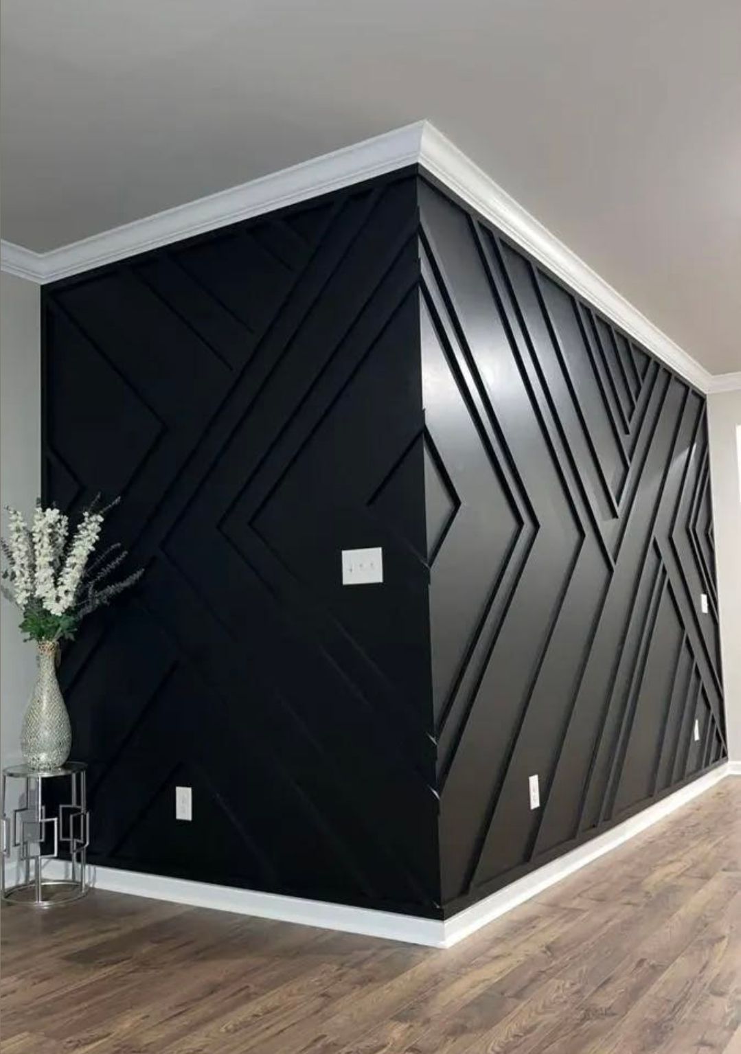 Black geometric accent wall in a modern room with white trim and wood flooring.