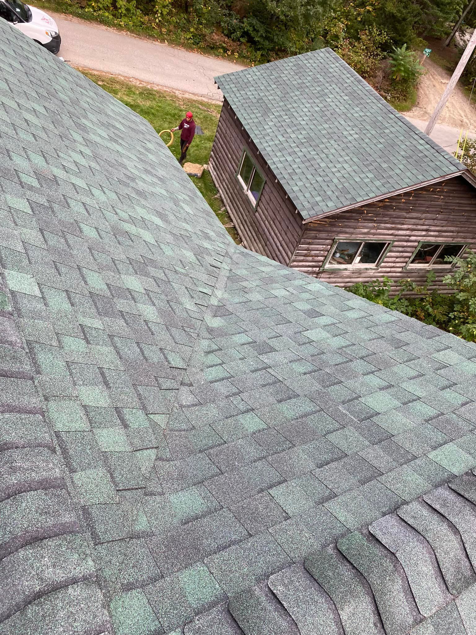 A person is standing on the roof of a house with a green roof.