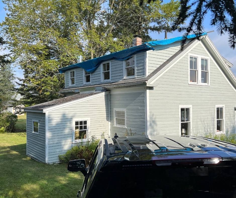 A truck is parked in front of a house with a blue tarp on the roof.