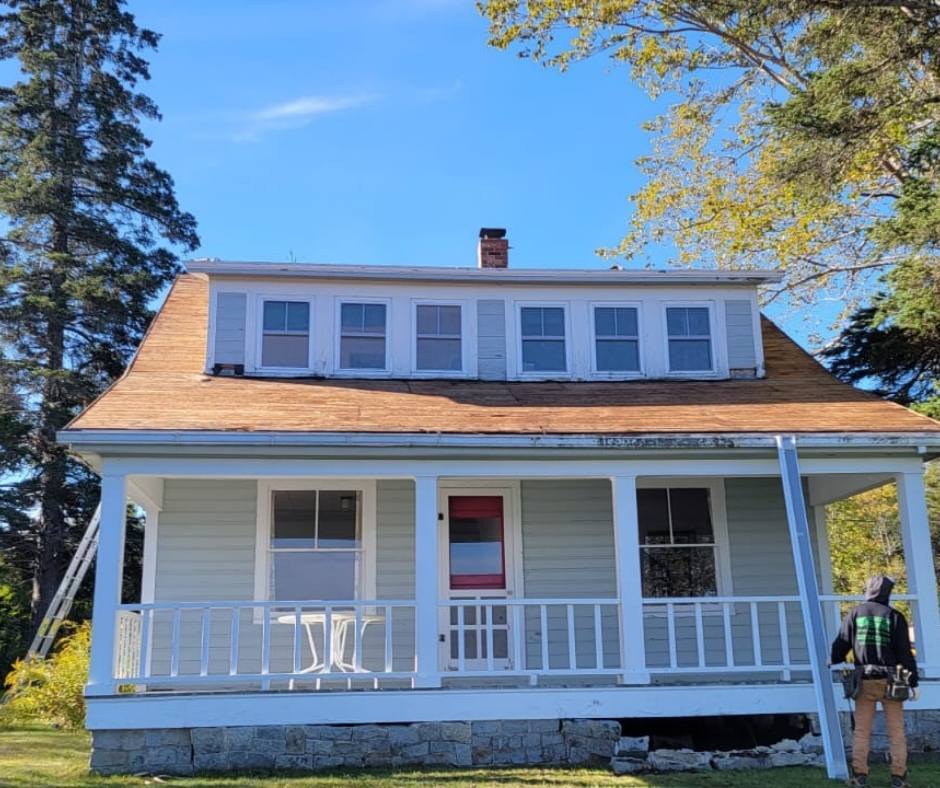 A man is standing on a ladder in front of a house with a porch.