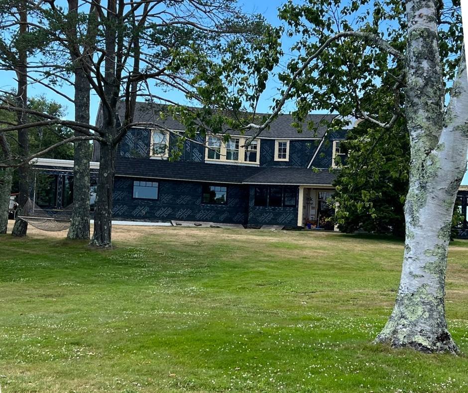 A large house is being built on a lush green field surrounded by trees.