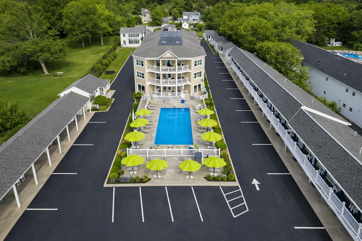 Aerial view of a hotel complex featuring a central swimming pool surrounded by lime green umbrellas and paved parking.