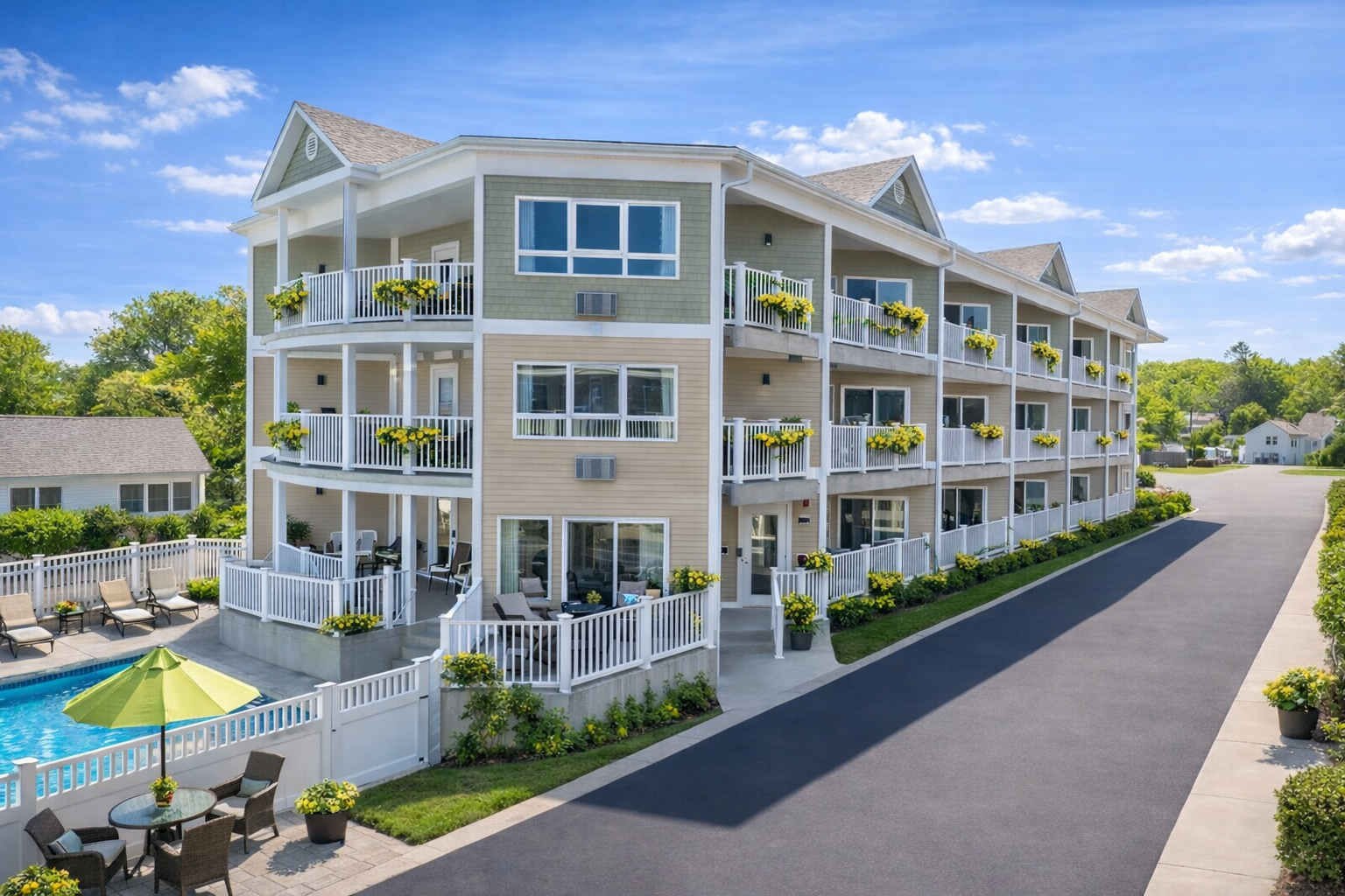 A modern, three-story hotel with tan and green siding, private balconies, and an adjacent swimming pool.
