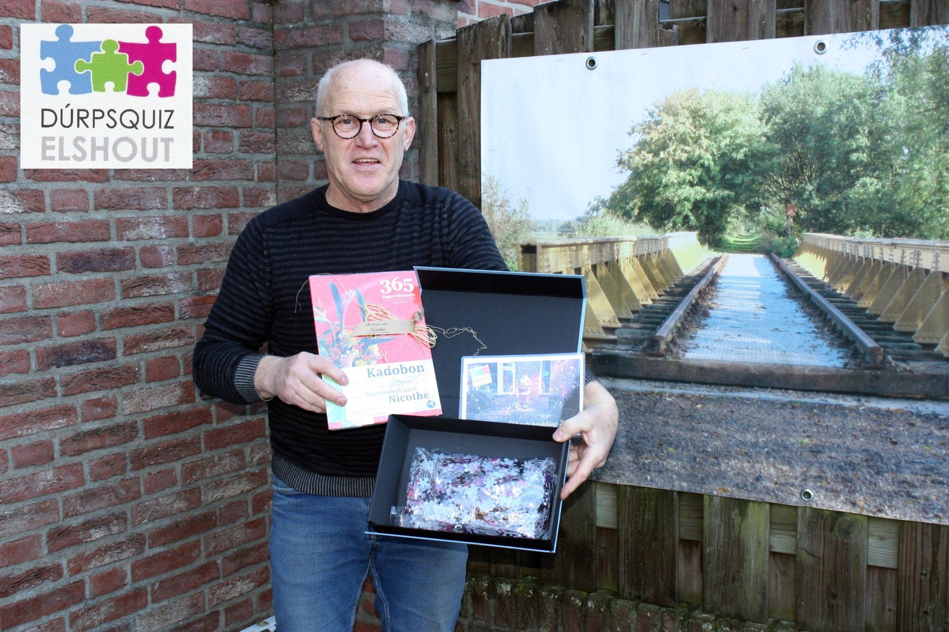 Een man met een boek en een doos staat buiten met een schilderachtig landschap op de achtergrond.