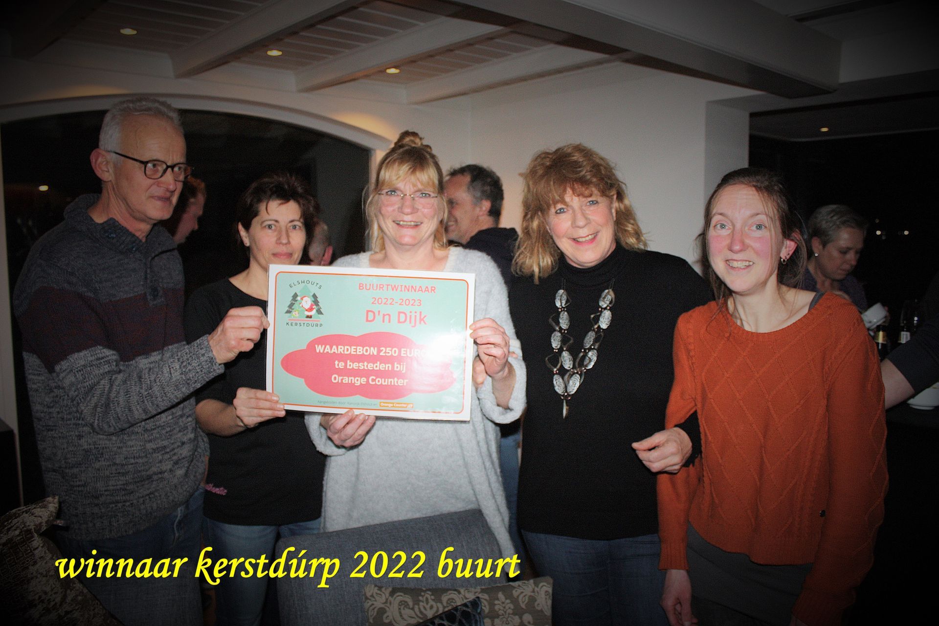 Een groep mensen houdt een winnend certificaat vast en viert feest tijdens een evenement. Donkere omgeving, overwegend casual kleding.