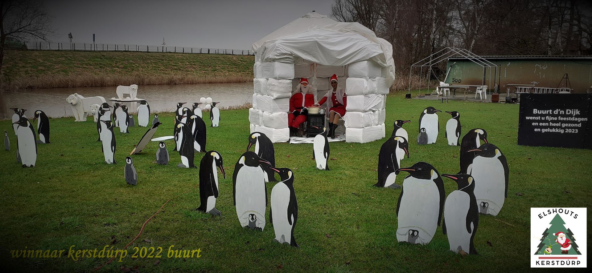 Een veld met uitgeknipte pinguïns omringt een tent waarin twee kerstmannen zitten.