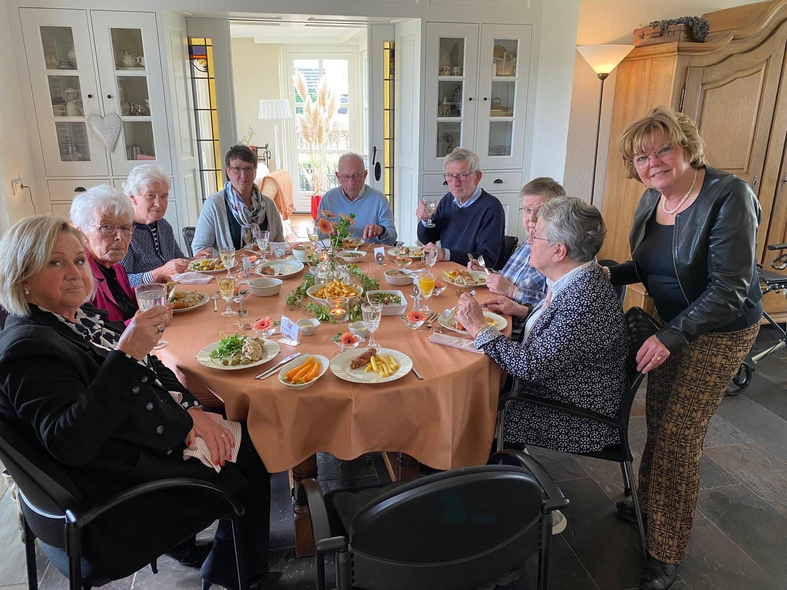 Een groep mensen zit aan een ronde tafel te eten en te praten in een eetkamer.