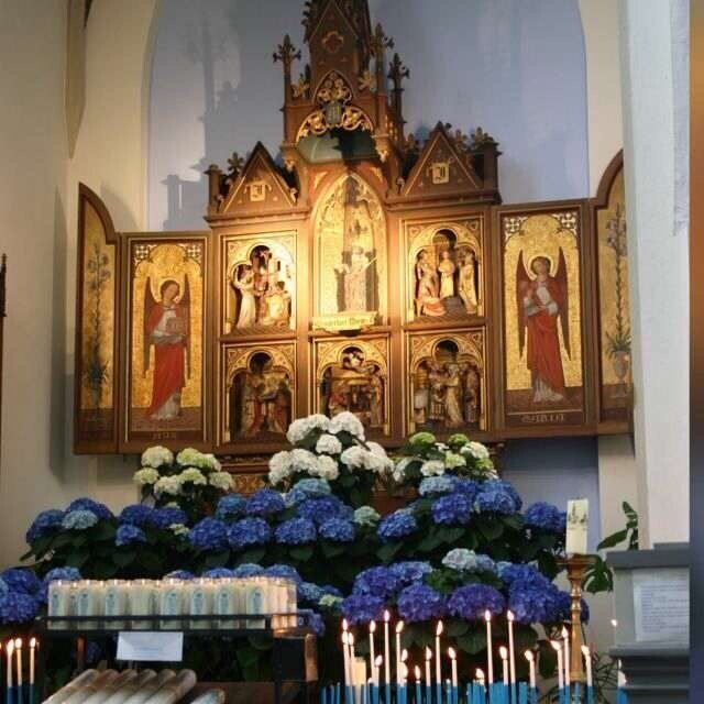Kerkaltaar met bloemen, kaarsen en een houten altaarstuk met religieuze figuren.