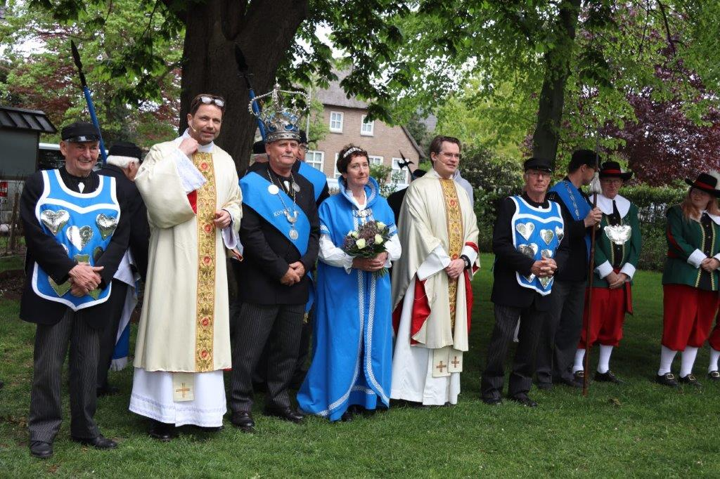 Een groep mensen in traditionele kleding staat buiten; twee van hen dragen religieuze gewaden, sommigen een vest.
