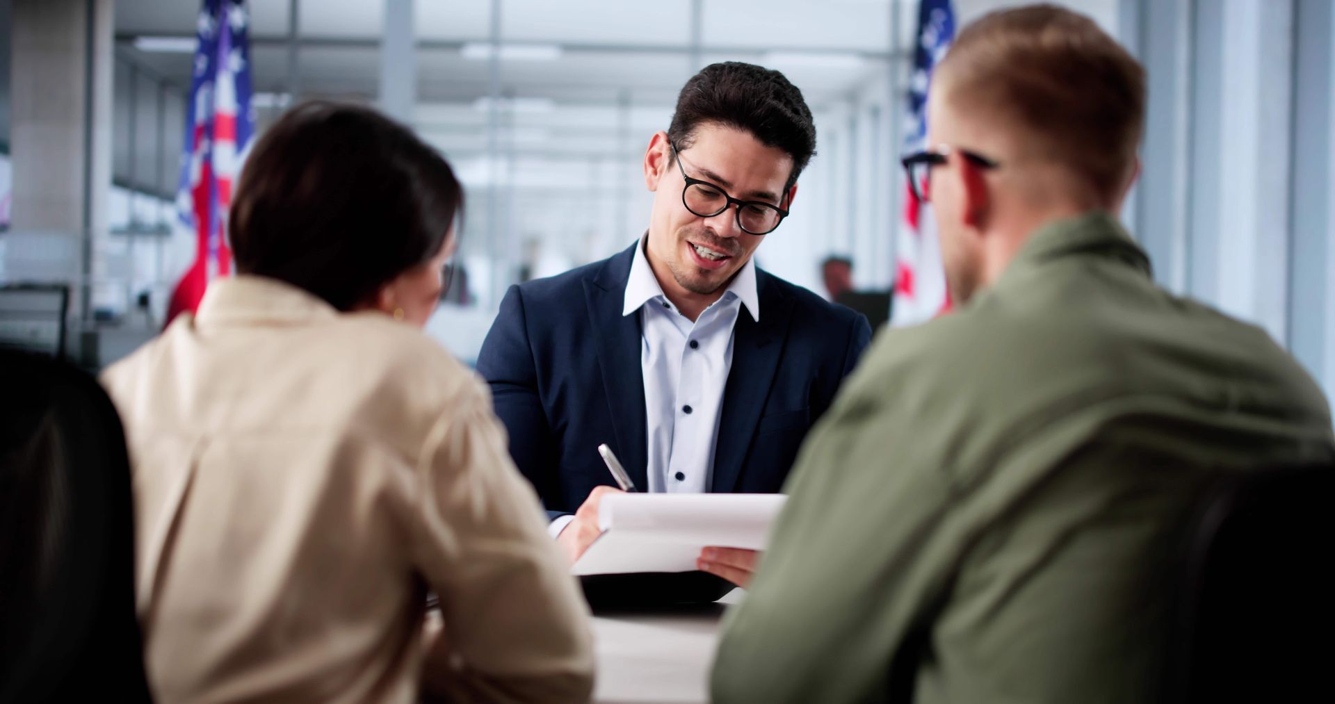 Business meeting in an office, with a man in a suit speaking to two seated colleagues.