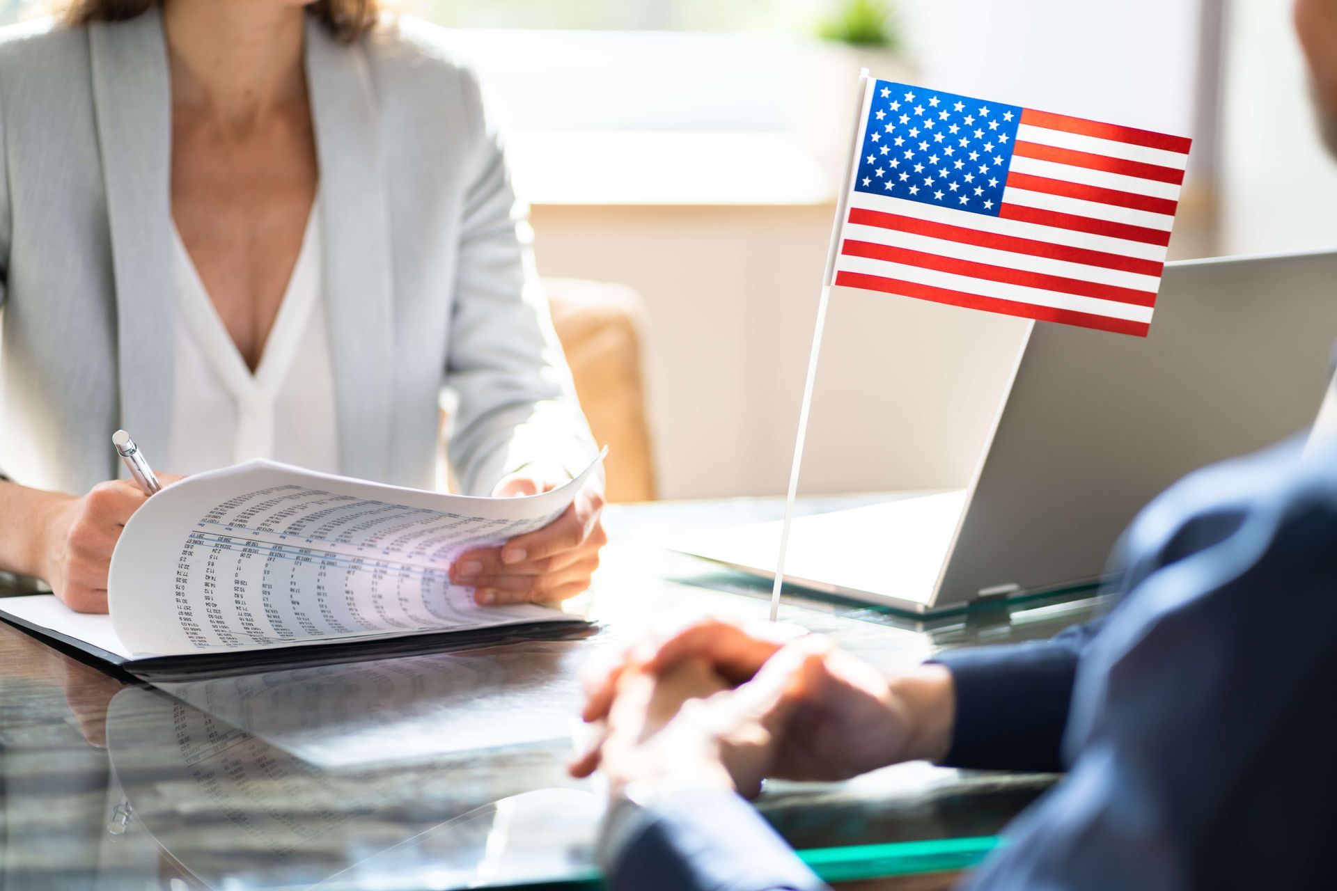 Office meeting with a woman reviewing documents beside a laptop and a small American flag