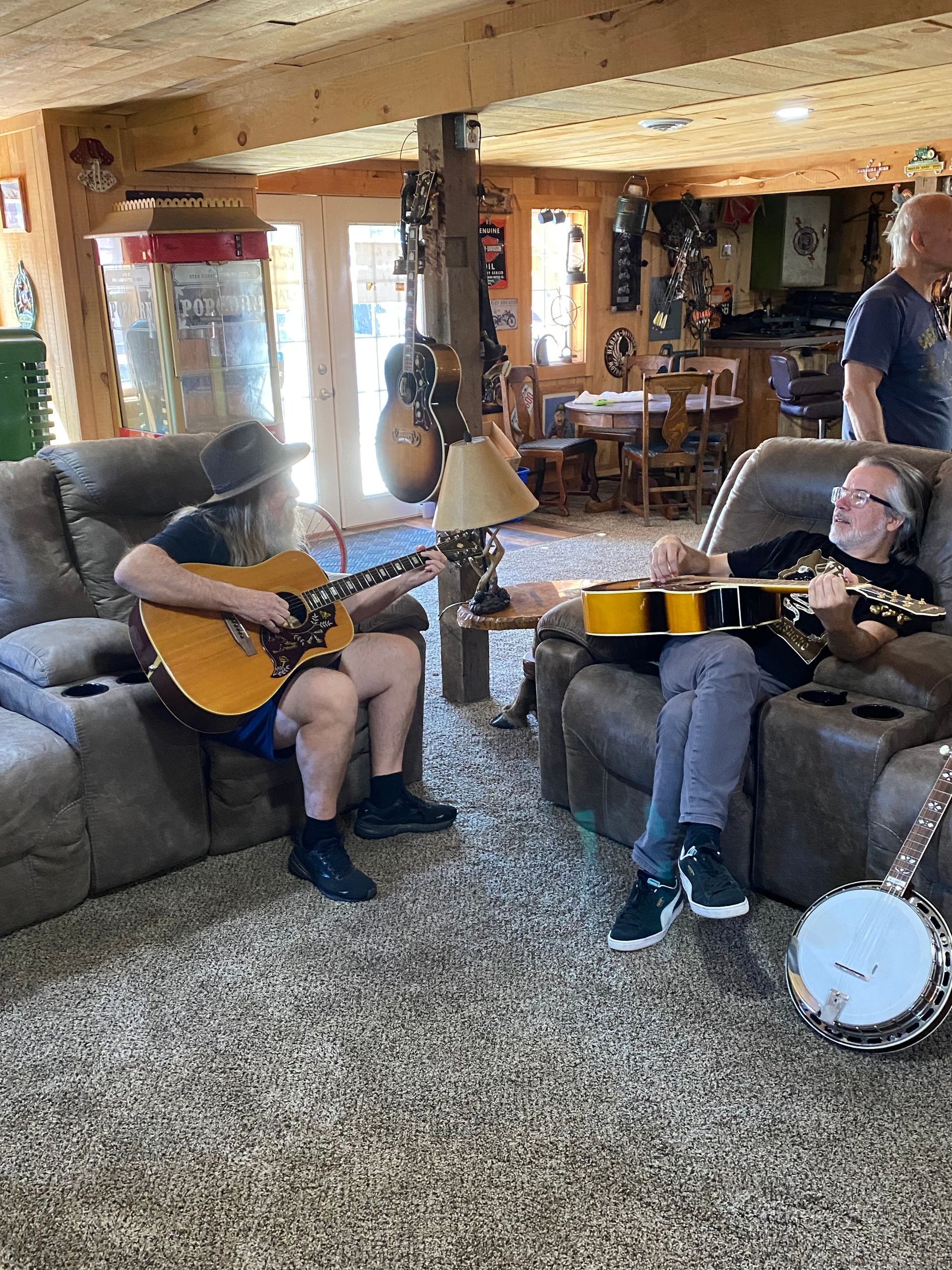 Two people playing guitars in a cozy living room, with a banjo on the floor and a couch nearby