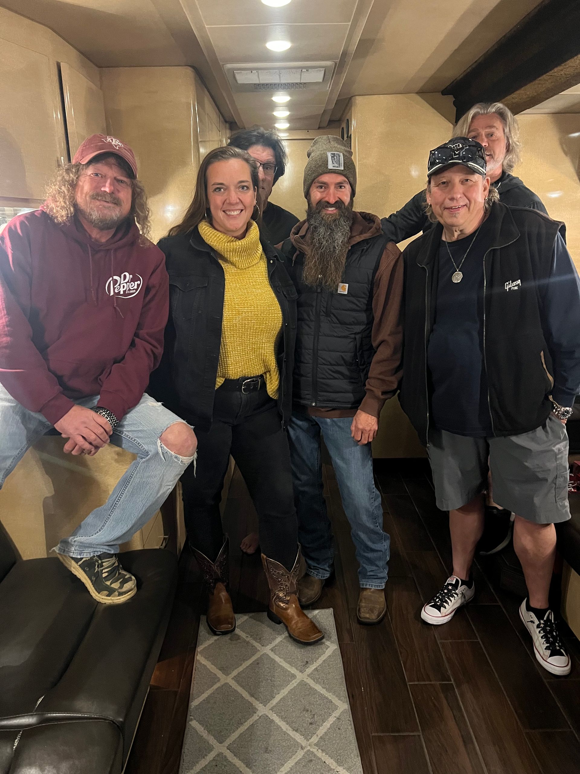 Four people posing together in a hallway, wearing winter hats and jackets, smiling at the camera.