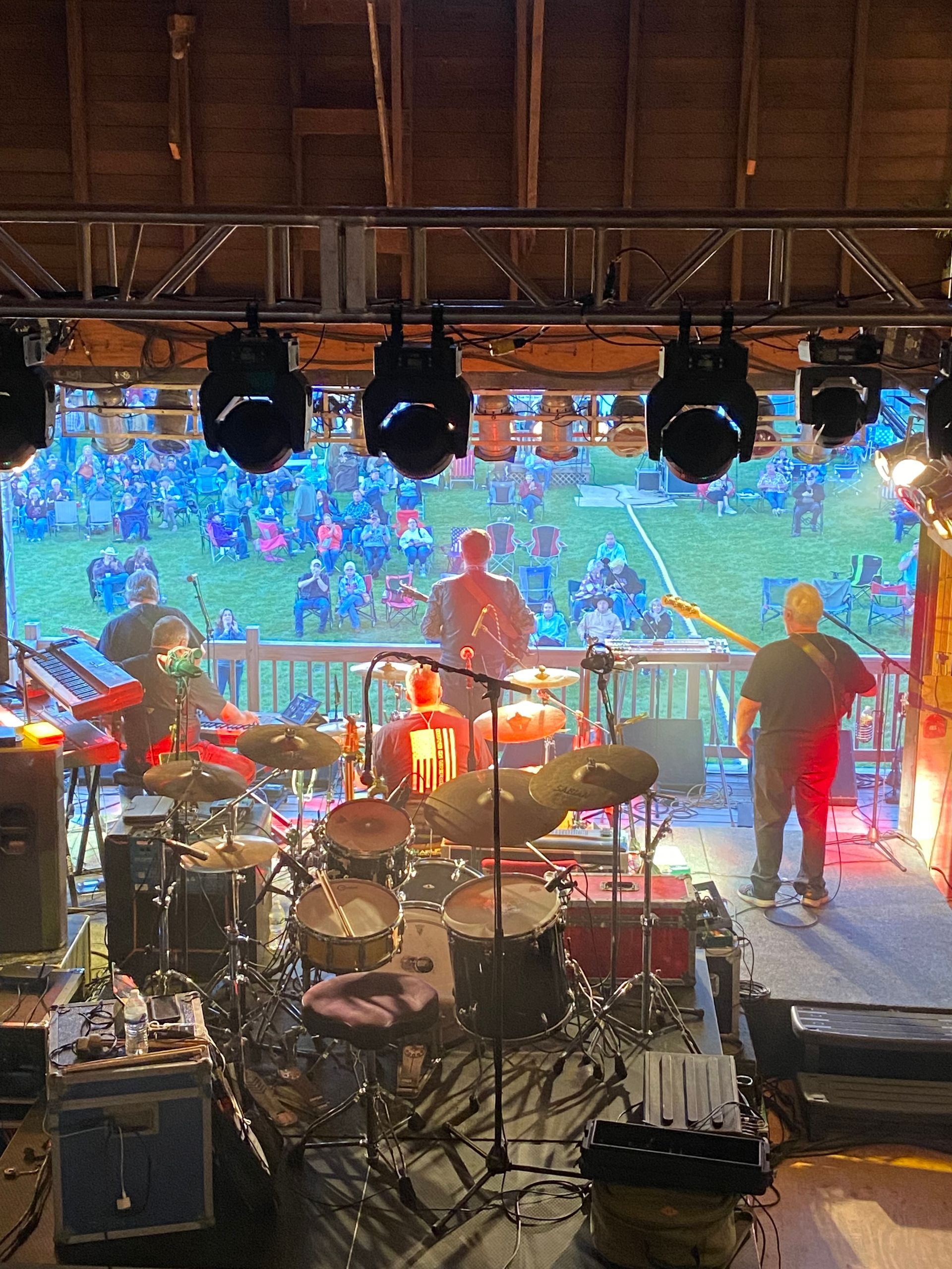 Stage view with drum kit, guitars, and hanging lights before a colorful outdoor crowd backdrop