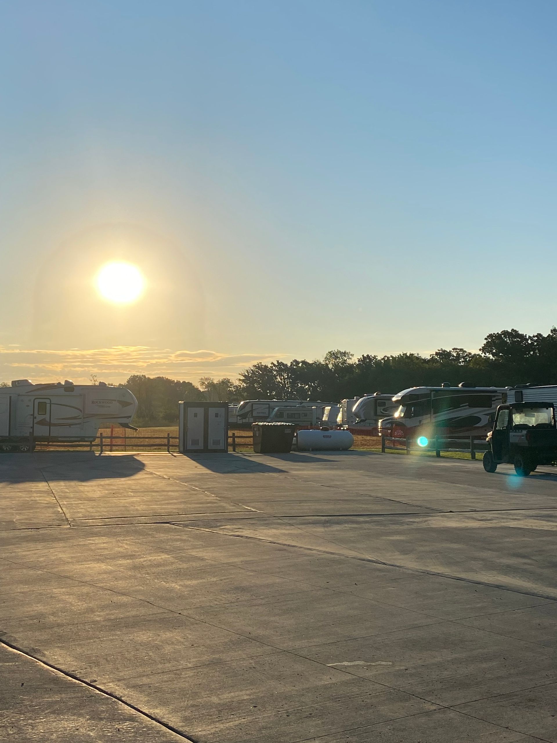 Sunlit parking lot with parked cars and trailers under a clear sky at sunrise