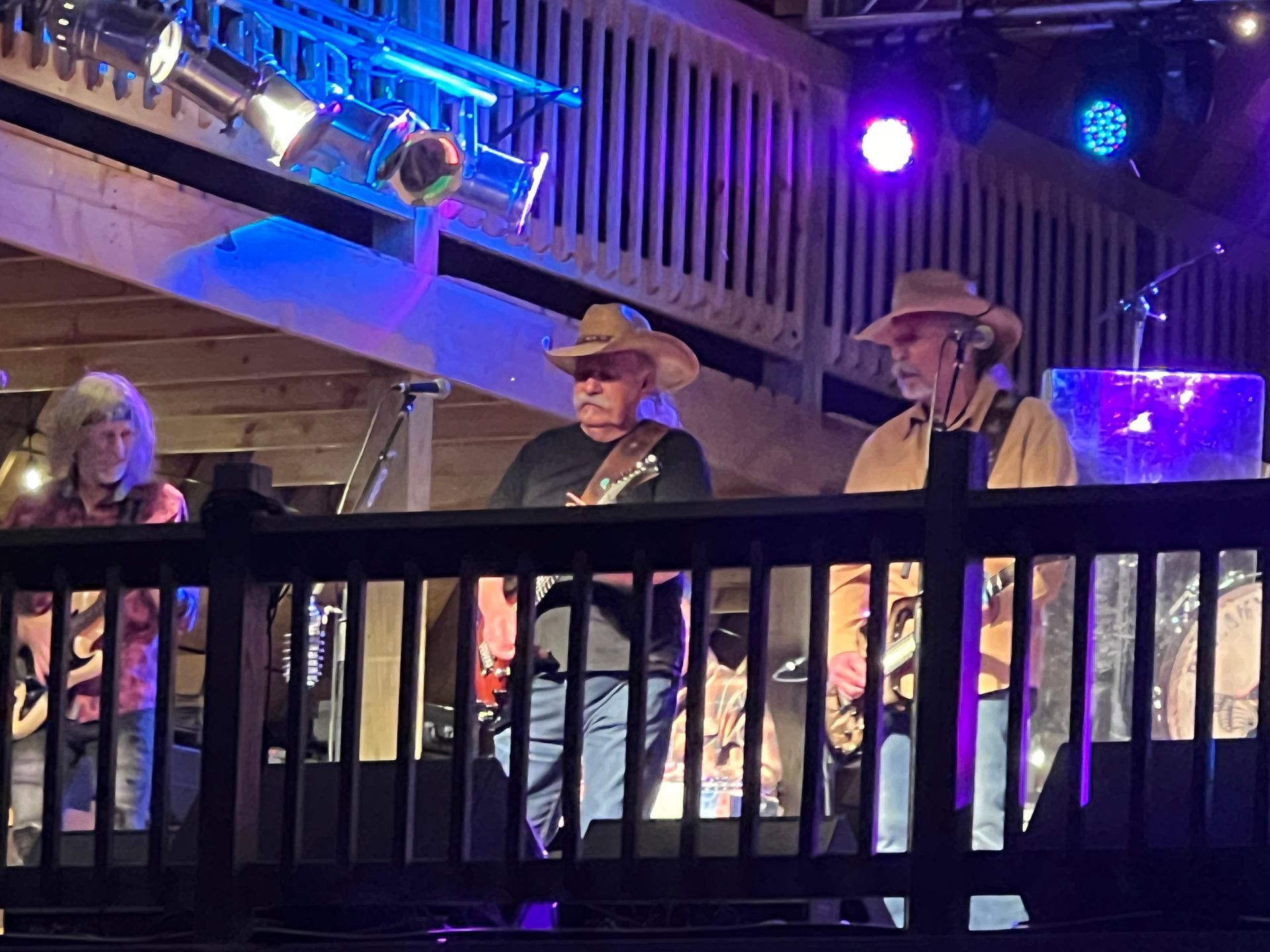 Three musicians in cowboy hats performing on a stage under purple and blue lights