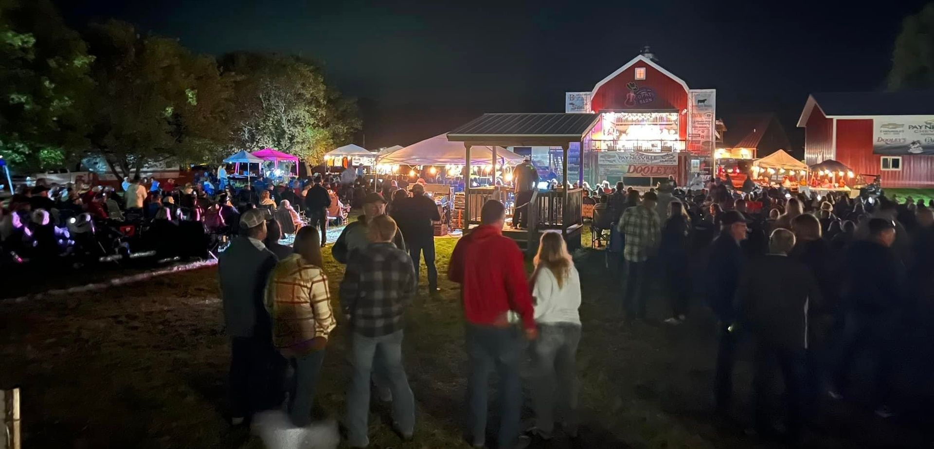 Crowded nighttime holiday festival with lights and a brightly lit building in the background