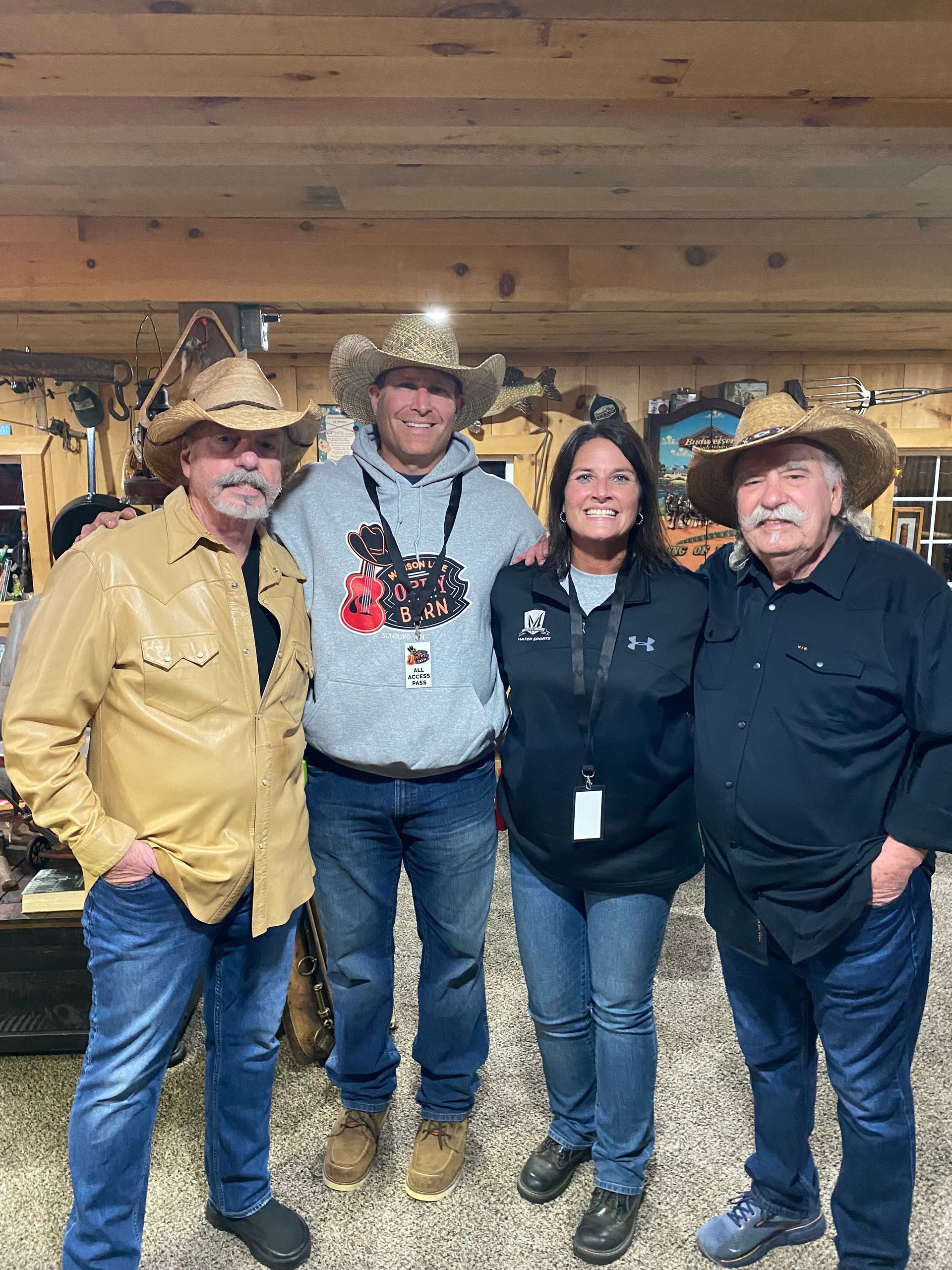 Four adults posing indoors in cowboy hats and Western attire with rustic wood decor behind them.