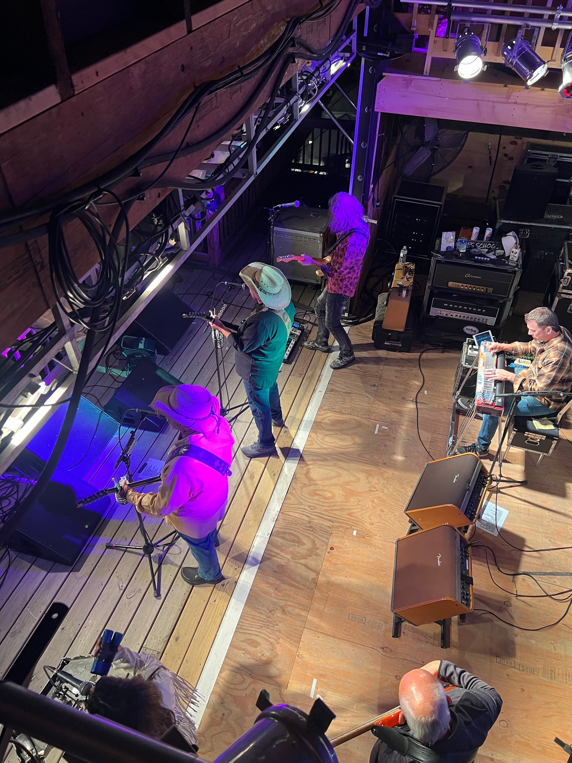Live music venue viewed from above, with performers and seated audience under purple stage lighting.