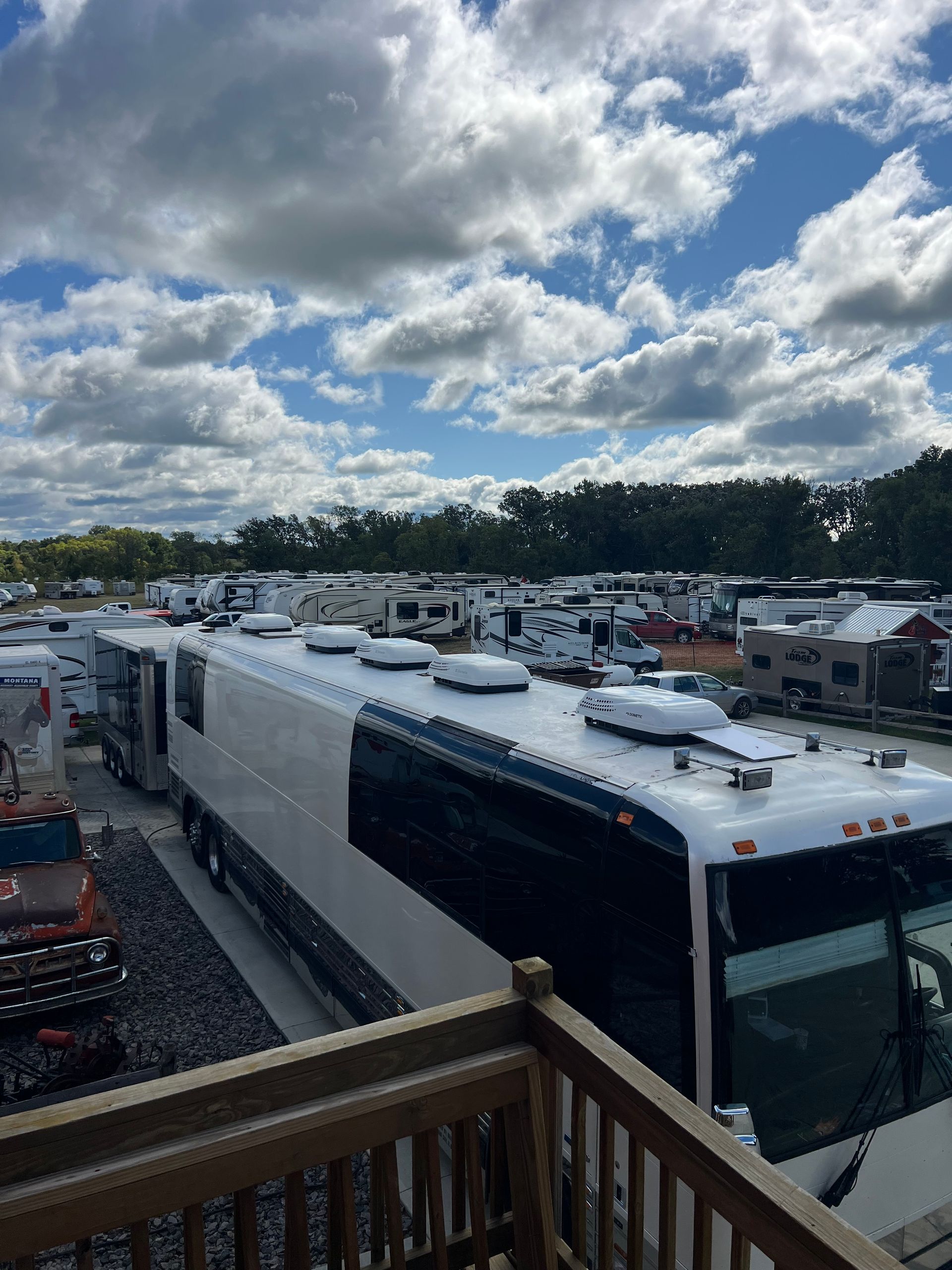 White coach bus in a parking lot under a cloudy sky, viewed from an elevated wooden deck.