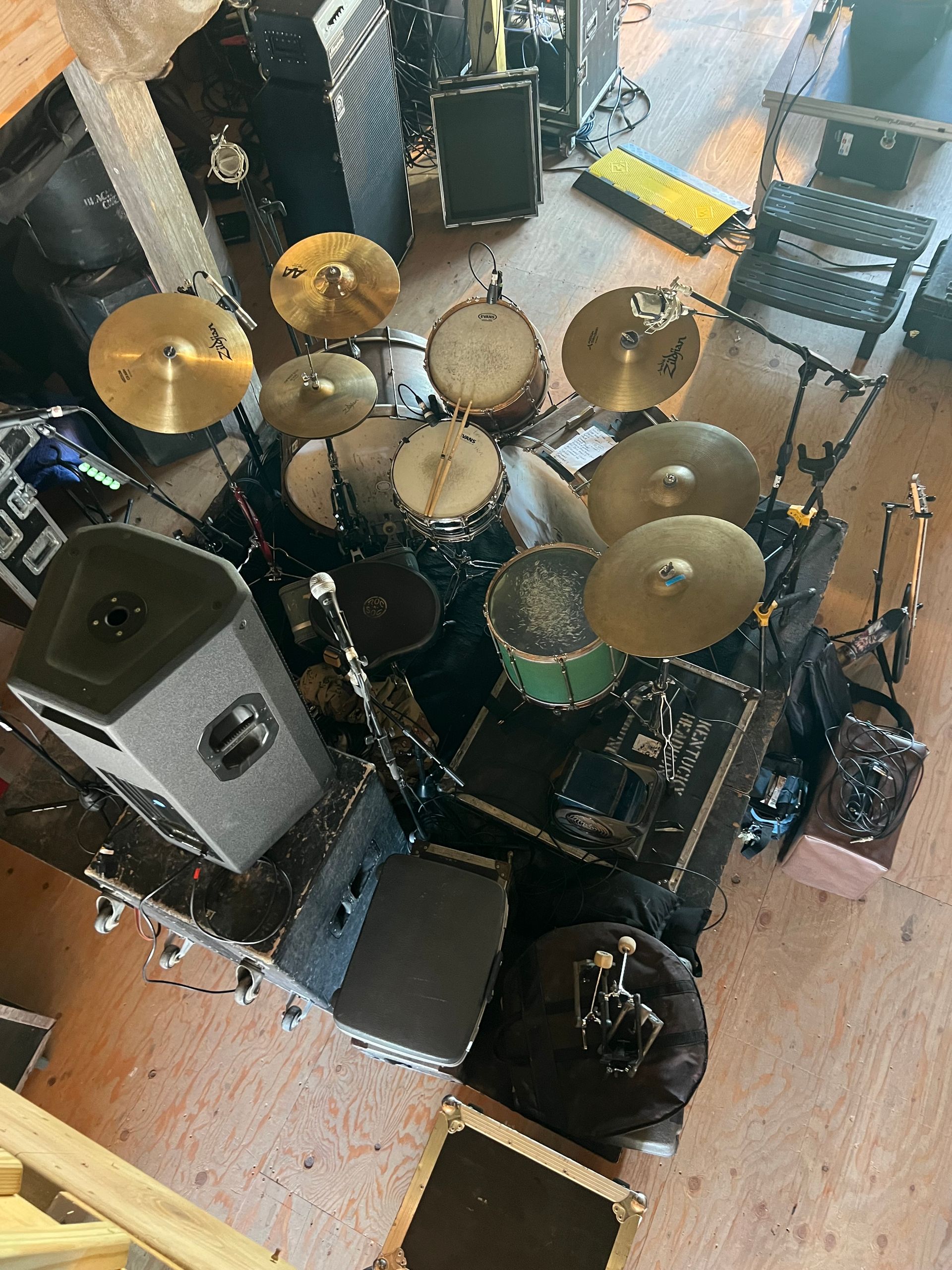 Overhead view of a drum kit in a small rehearsal room with amps, stands, and cables on the floor