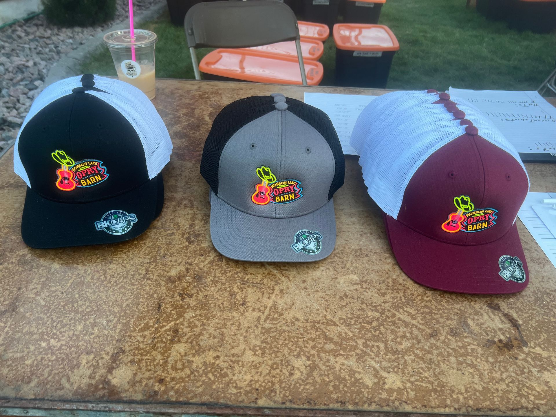 Three colorful baseball caps with butterfly patches displayed on a table outdoors.