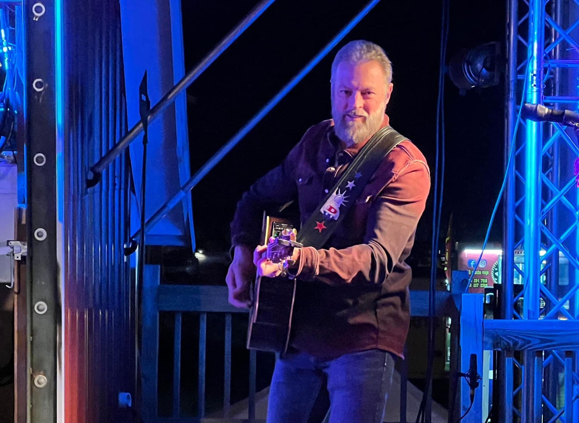 Man playing acoustic guitar on a blue-lit stage with metal truss lighting