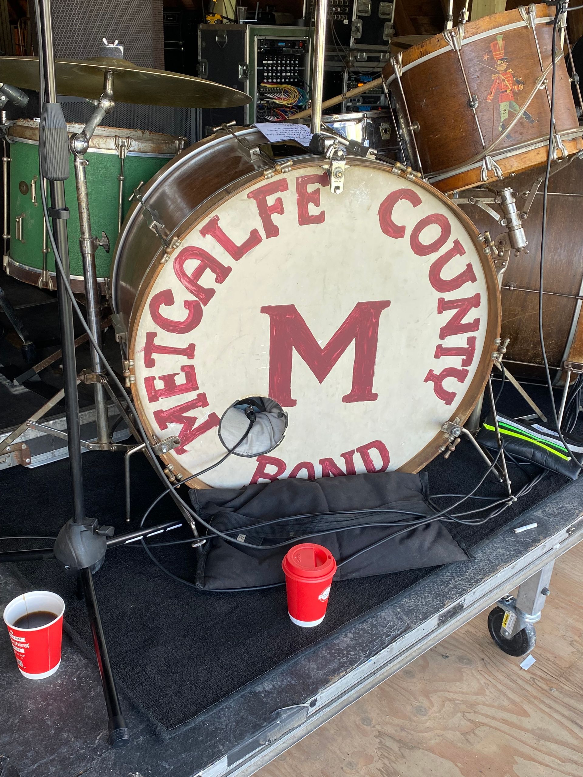 Vintage drum kit with a bass drum labeled “M” and “Mitcalae County Band” on a stage, with red cups nearby