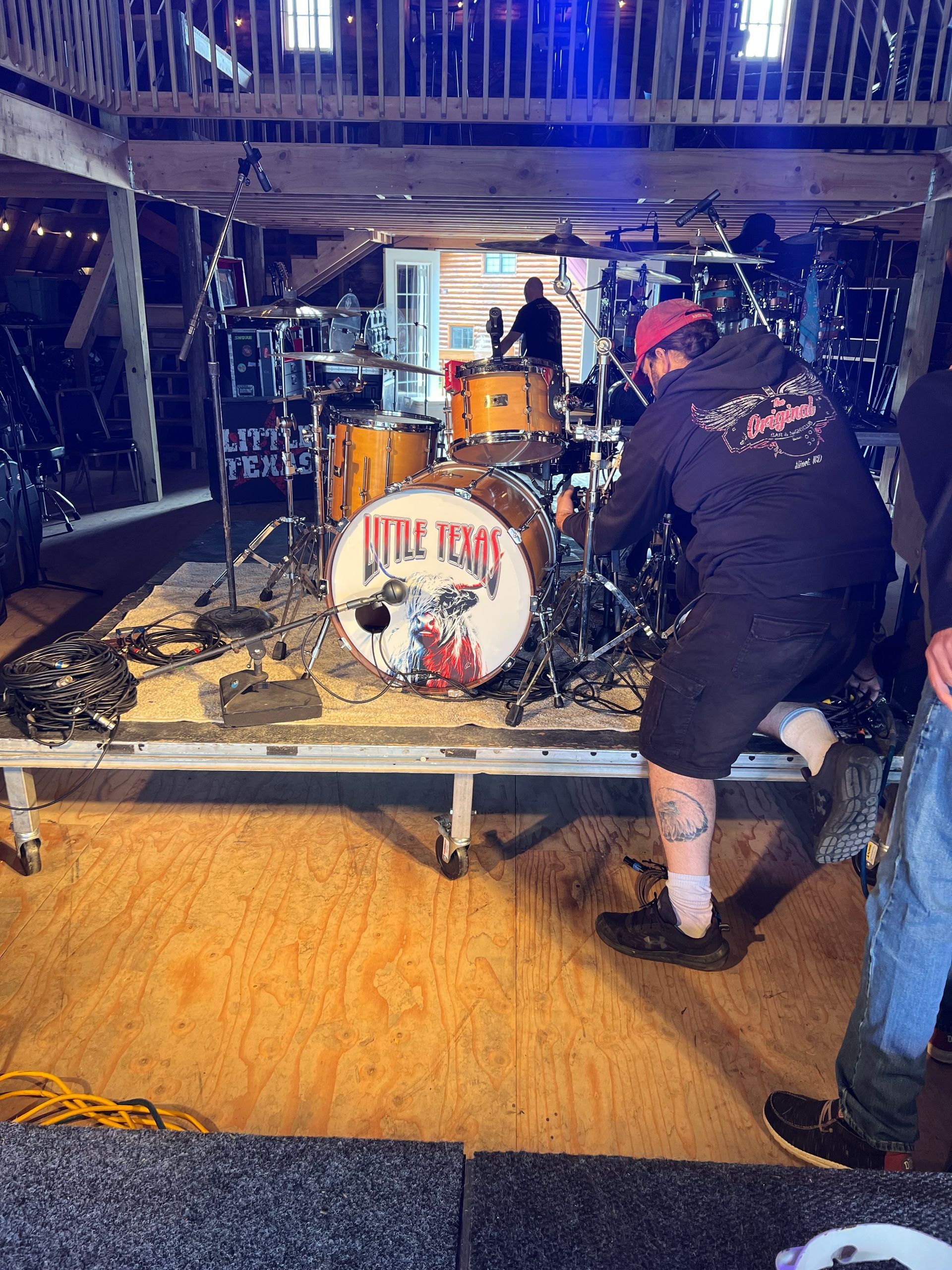 Band setup on a dimly lit stage, with a drum kit and a person adjusting equipment.