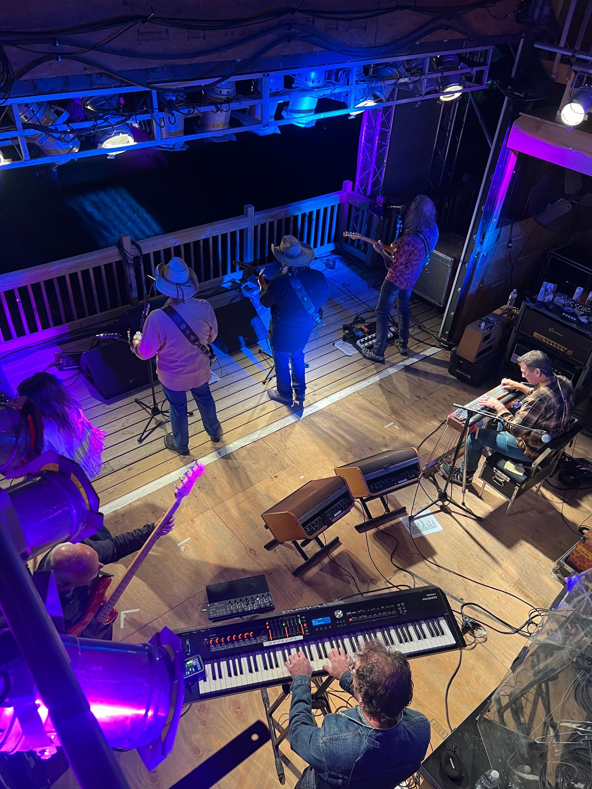 Band rehearsing on a stage with blue and purple lights, instruments, and musicians seen from above