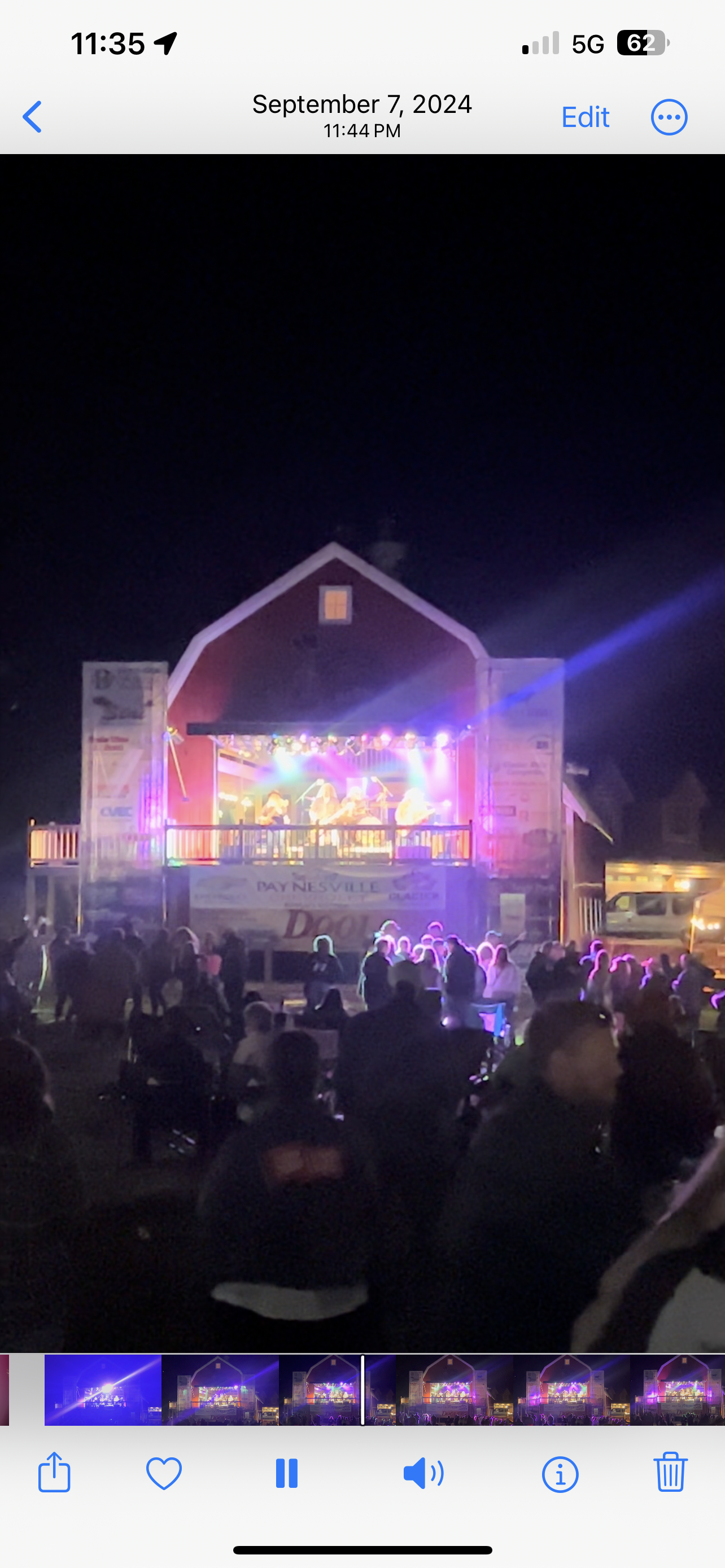 Outdoor concert at night with a brightly lit stage and a crowd of seated spectators in front.