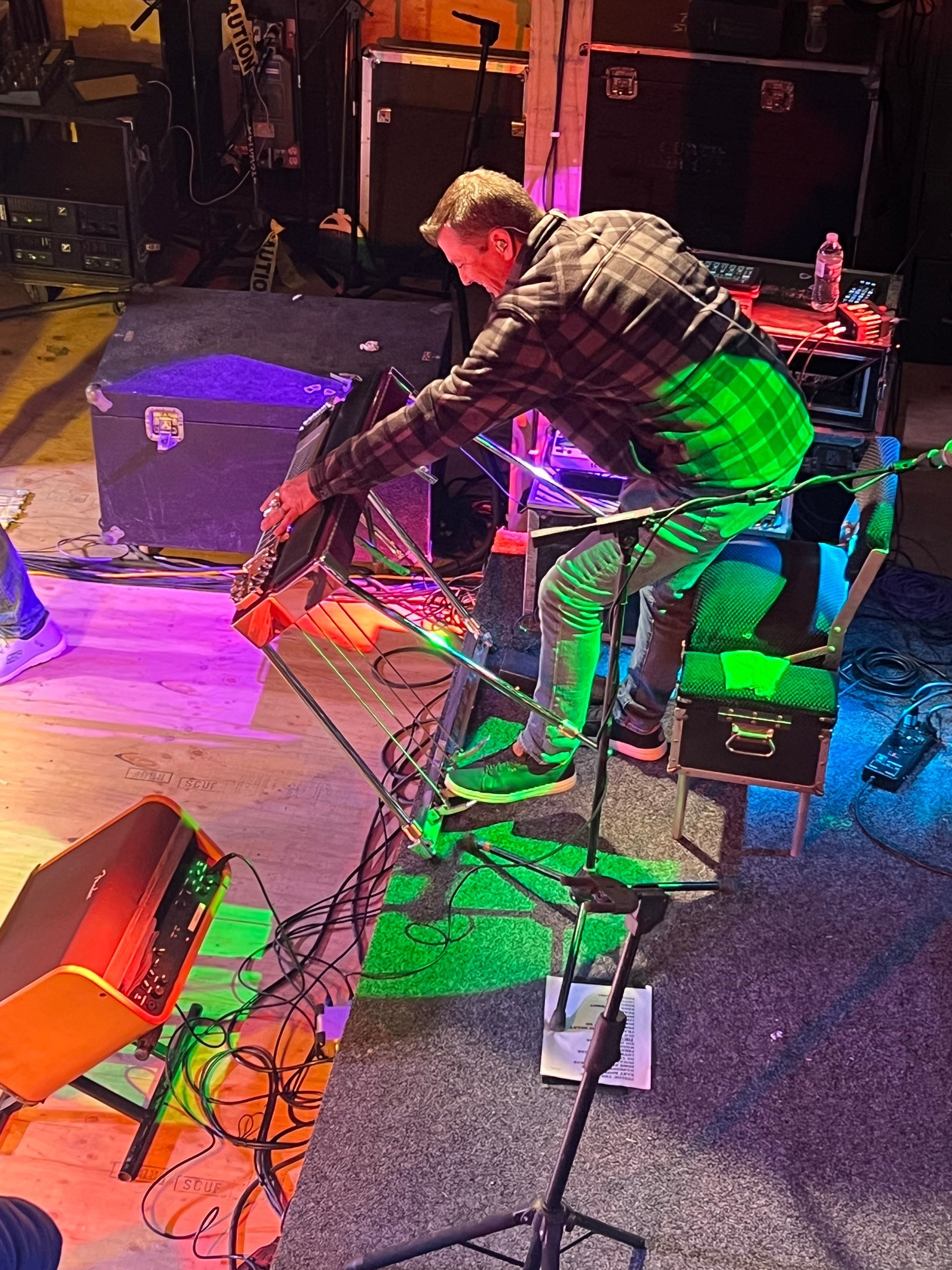 Person adjusting cables on a stage floor lit with colorful purple, green, and orange lights