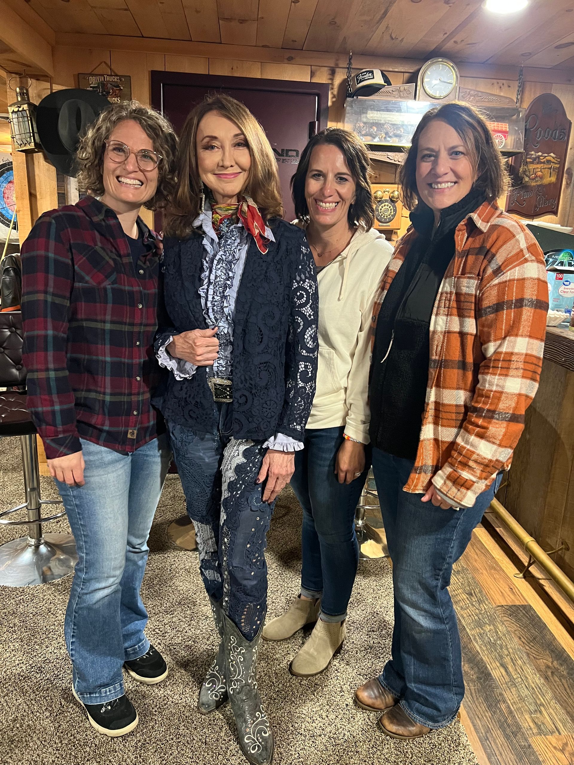 Four people smiling in a rustic cabin, standing side by side in flannel shirts and jeans.