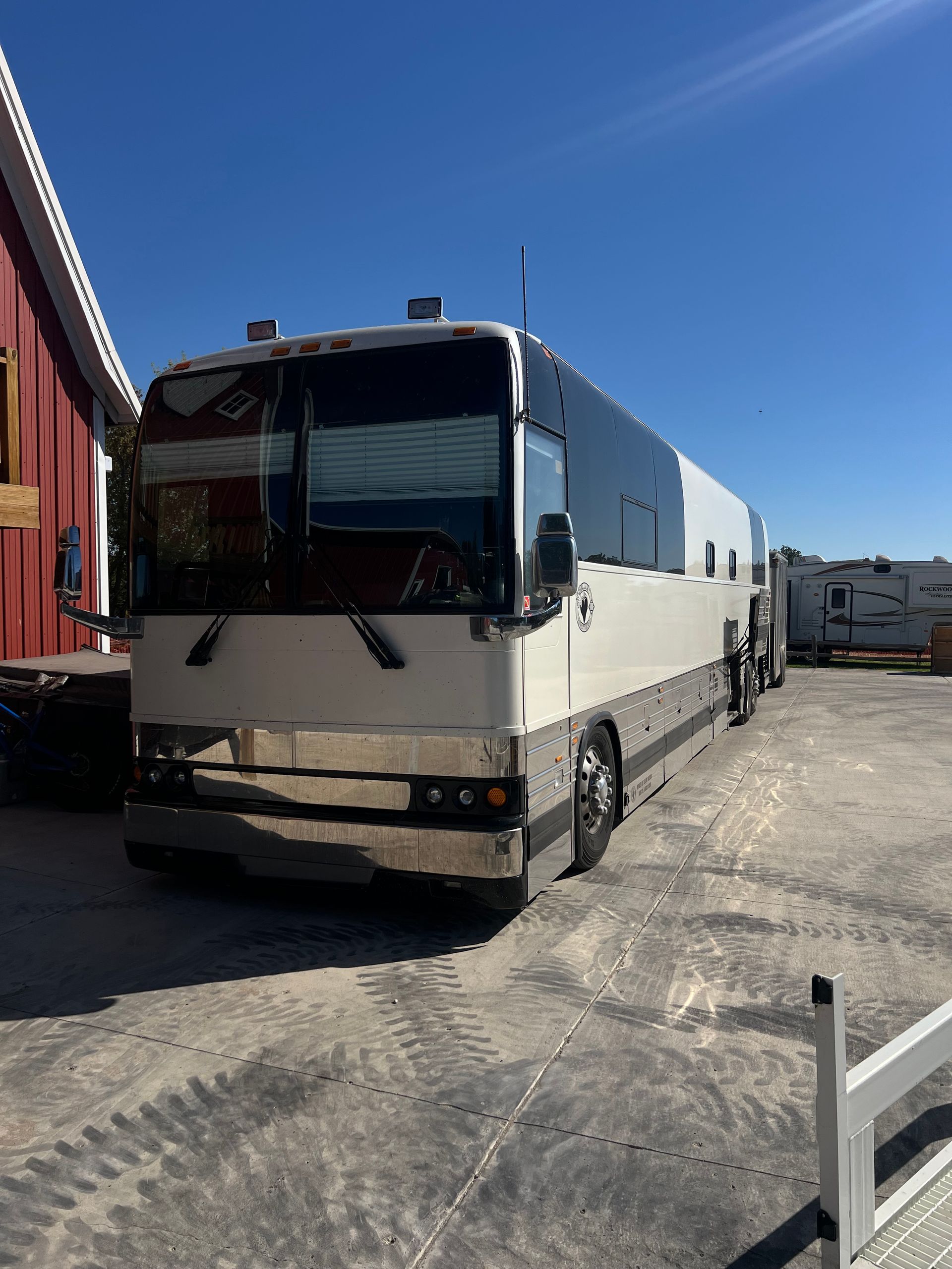 White bus parked in an industrial lot beside a red building under a clear blue sky