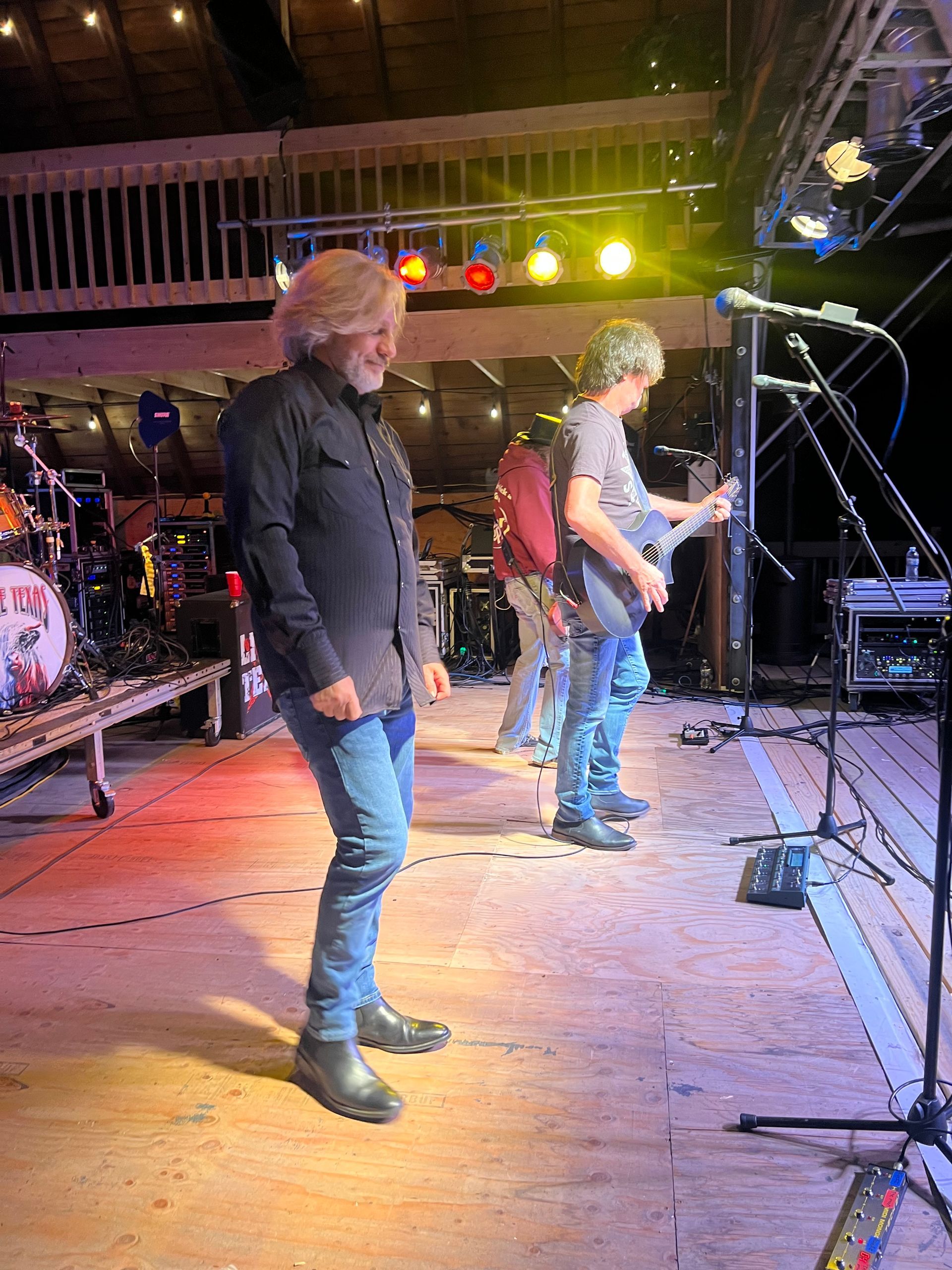 Band performing onstage under colorful lights, with a singer at the microphone and a guitarist beside him.