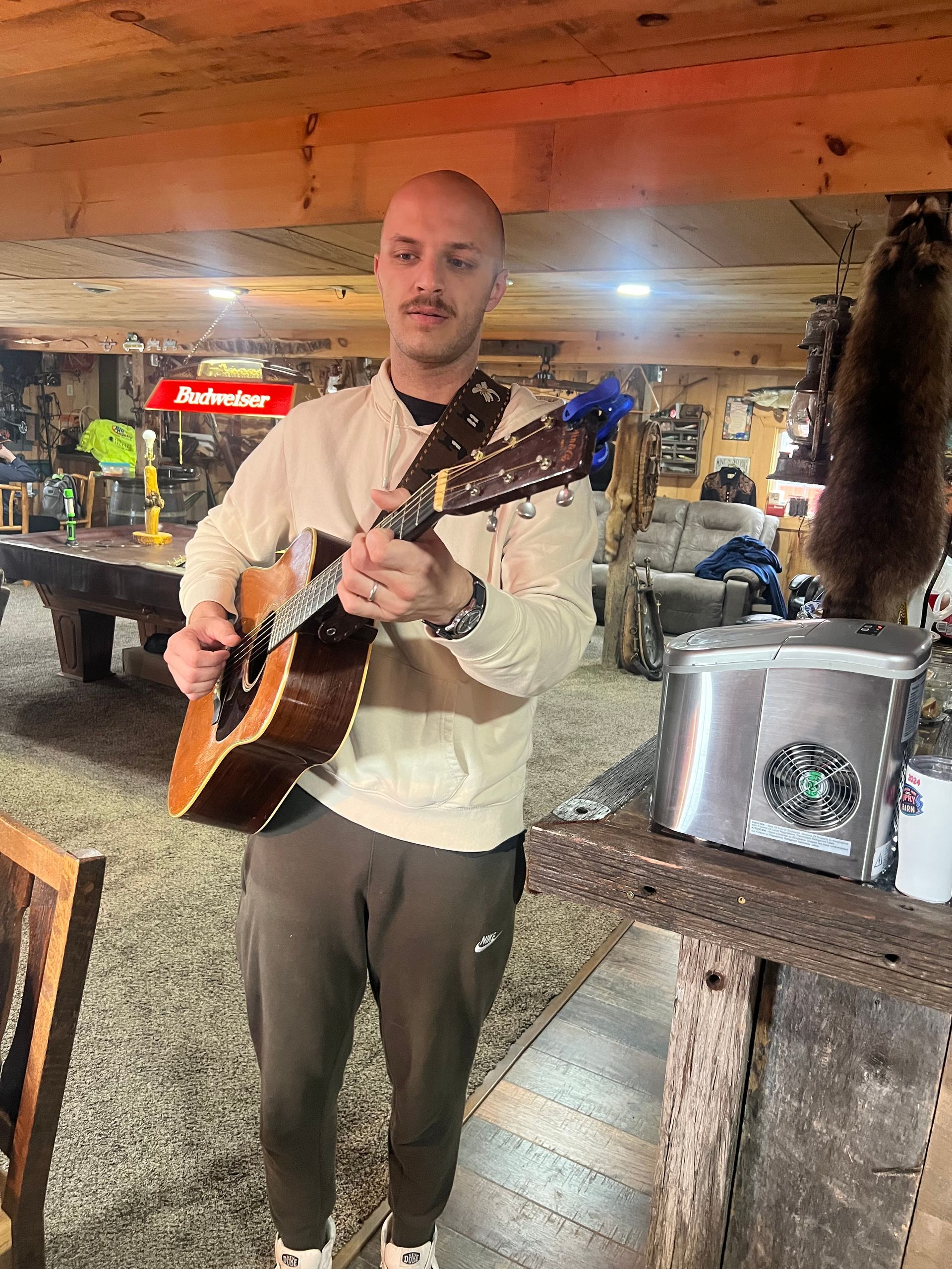 Man playing guitar in a rustic bar with mounted fish and warm wooden decor