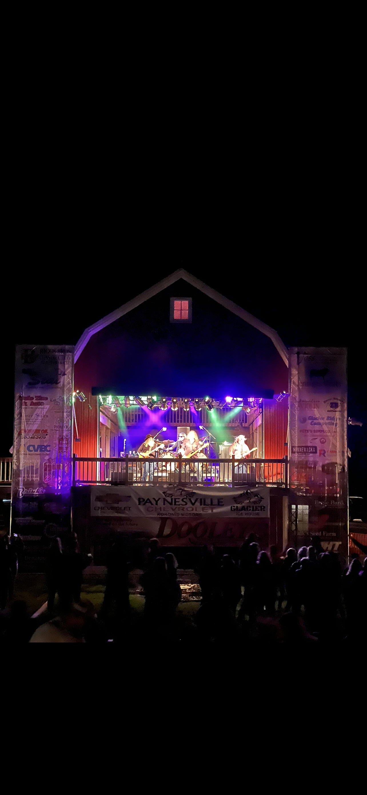 Nighttime outdoor concert with a brightly lit stage and performers under colorful lights