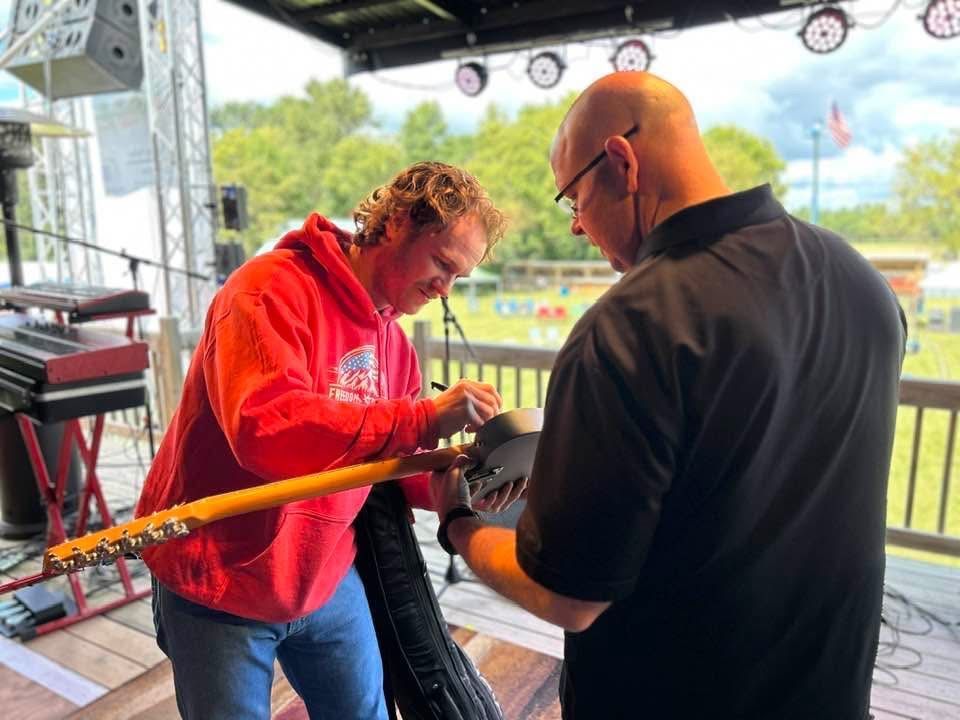 Two people at an outdoor stage adjusting equipment near a red barrier tape