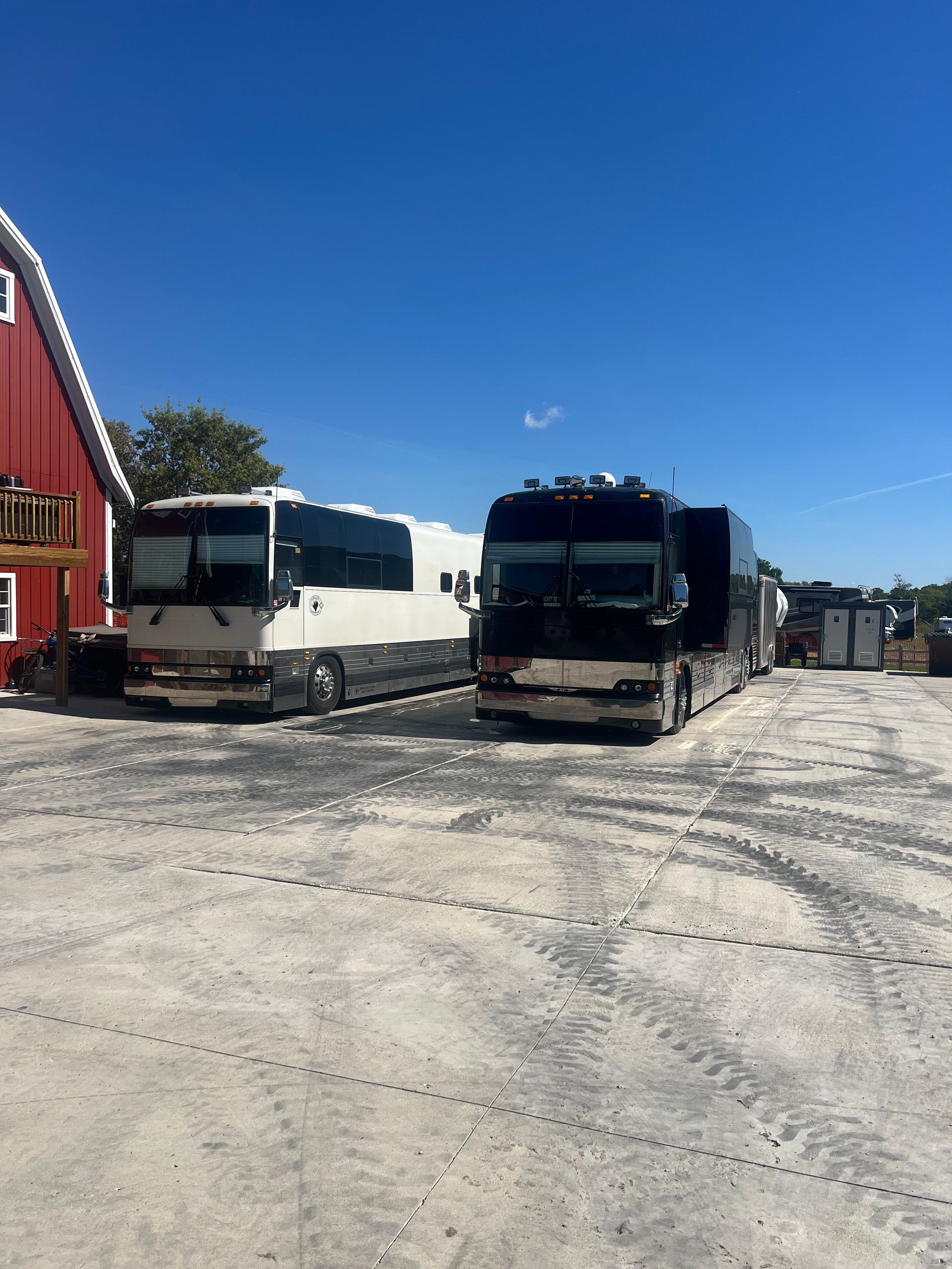 Two large trucks parked on a gravel lot beside a red building under a clear blue sky
