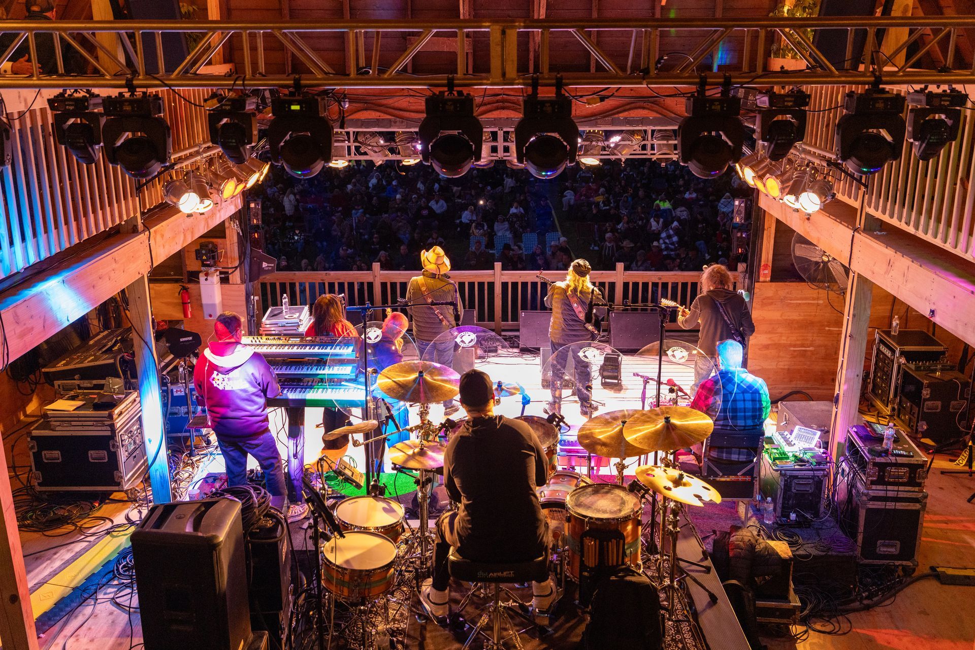 Live band performing on a brightly lit stage with drums, guitars, and colorful concert lighting