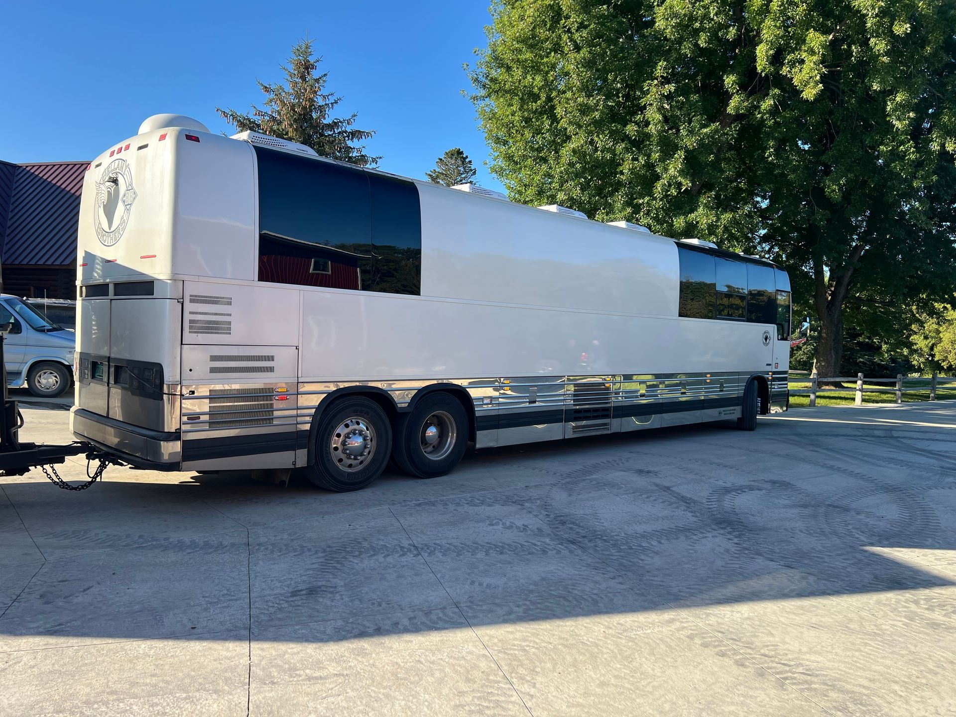 White tractor-trailer parked on a gravel lot beside trees and a building under a clear blue sky