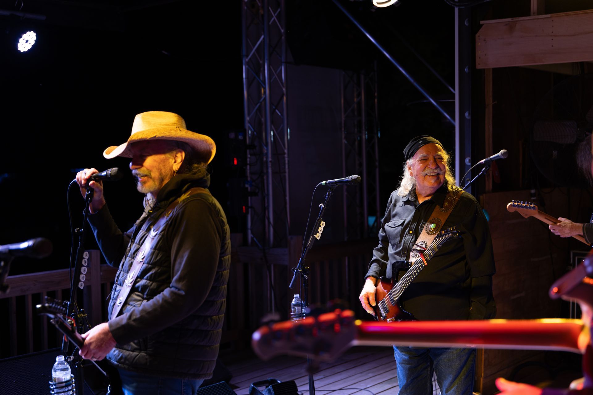 Live band performing on a dimly lit stage, with a musician in a yellow hat singing into a microphone.