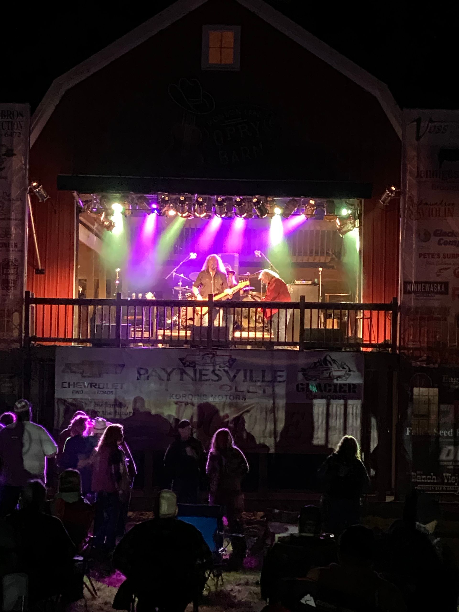 Outdoor stage concert at night with purple lights and a crowd in front
