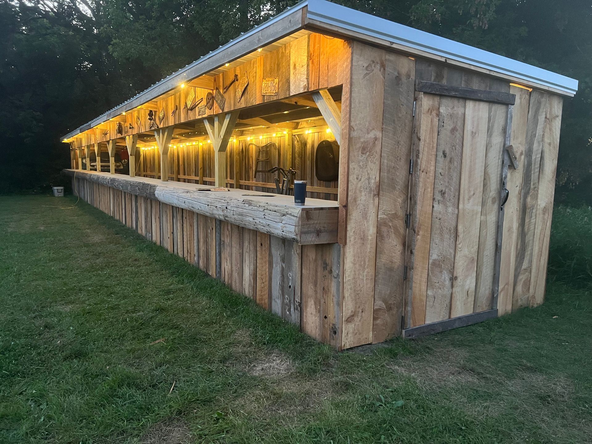 Rustic wooden outdoor bar with warm string lights along the side at dusk