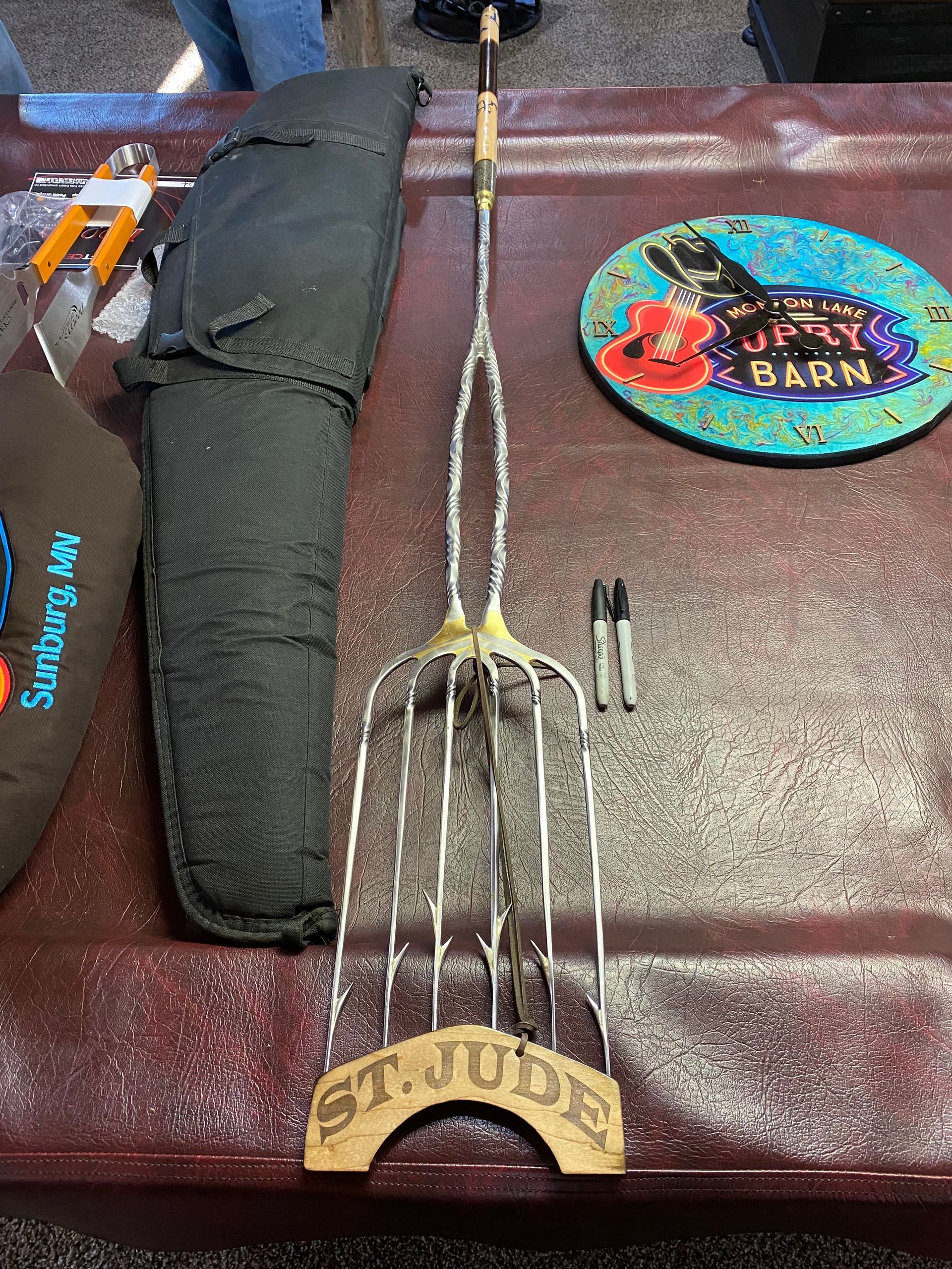 Banjo on a maroon tabletop beside a black case and round cowboy hat with a Barn patch