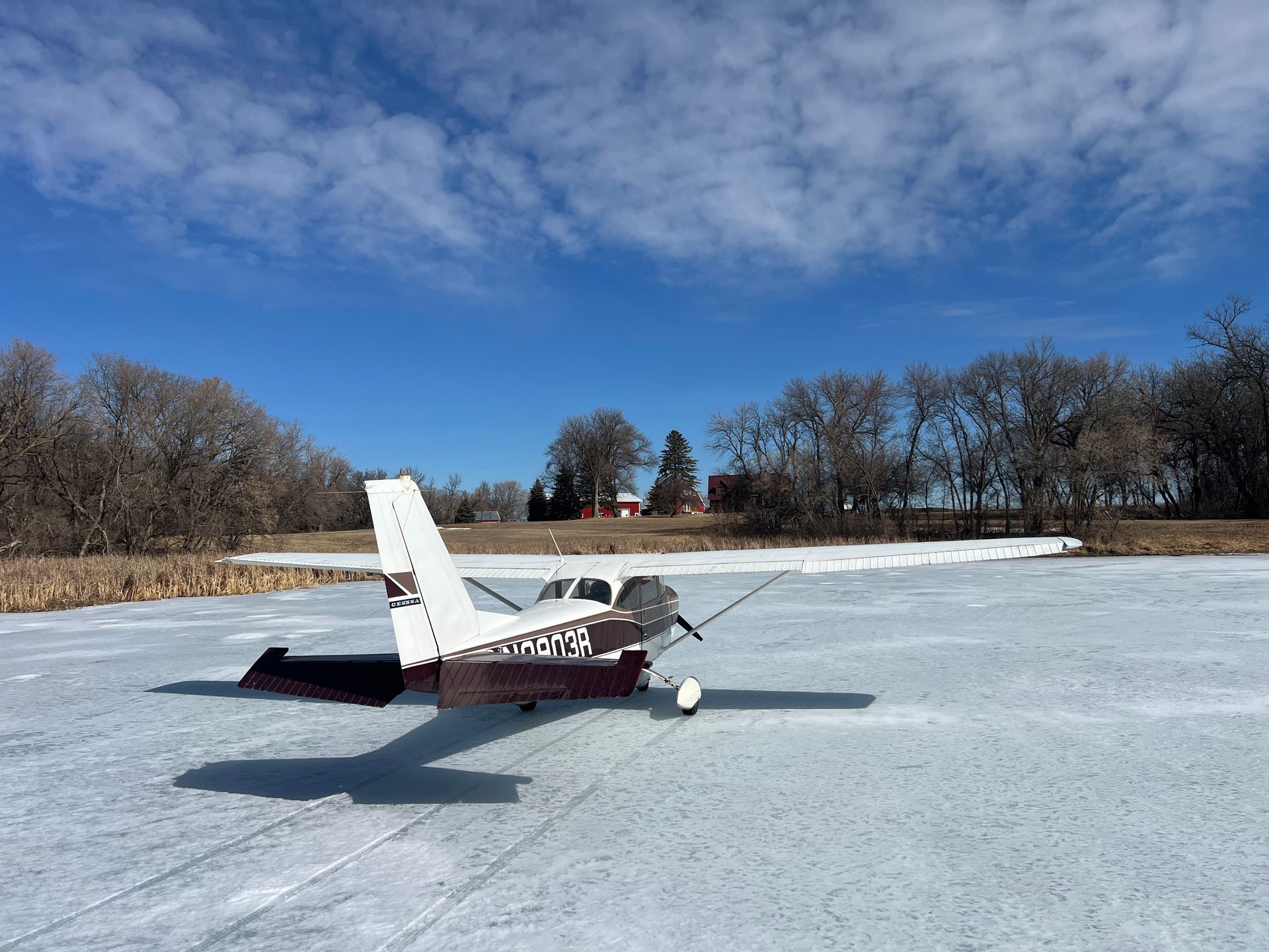 Small white-and-red airplane parked on a snowy airfield under a blue sky